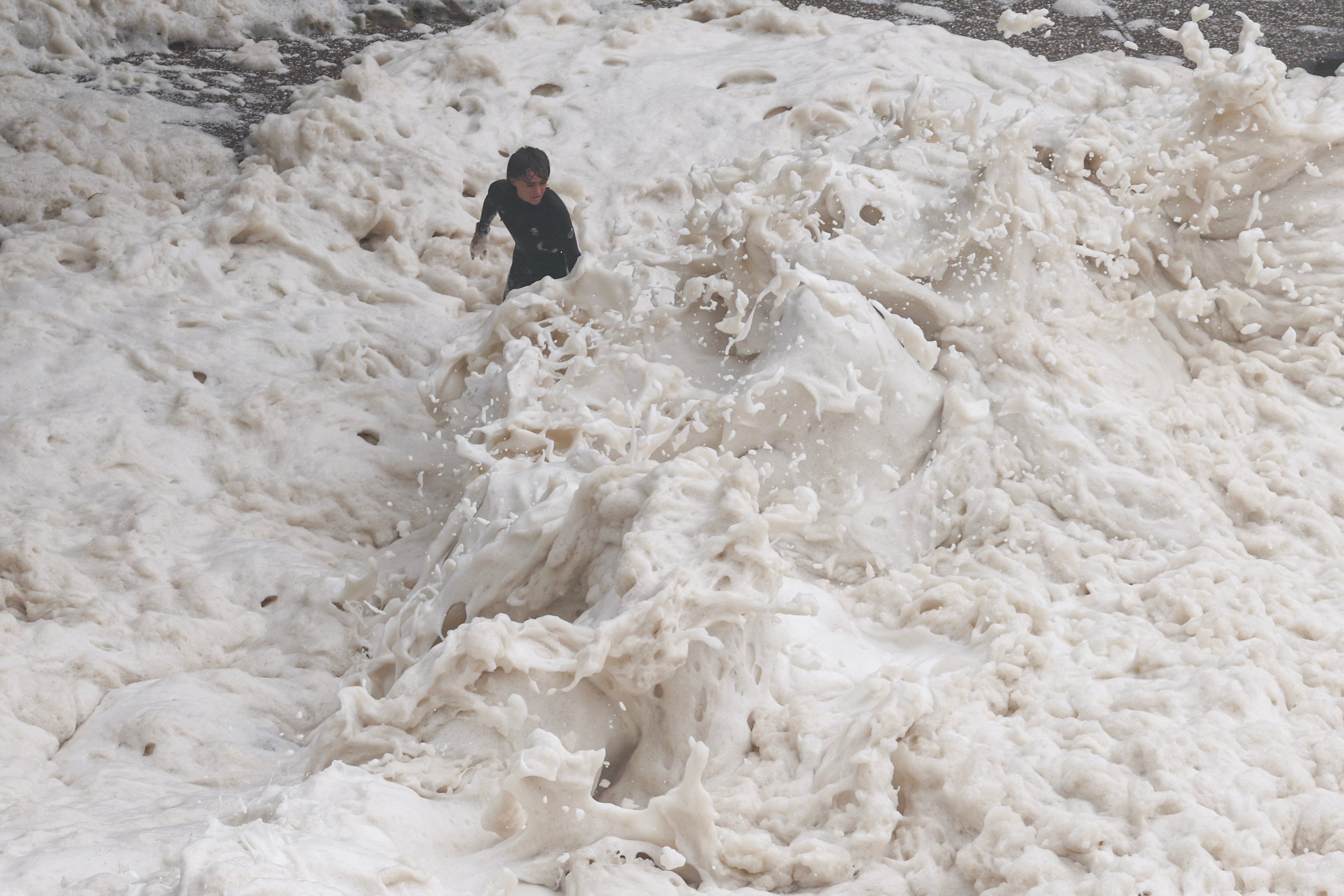 Young men play in sea foam created by record-breaking waves as the outer fringe of Tropical Cyclone Alfred