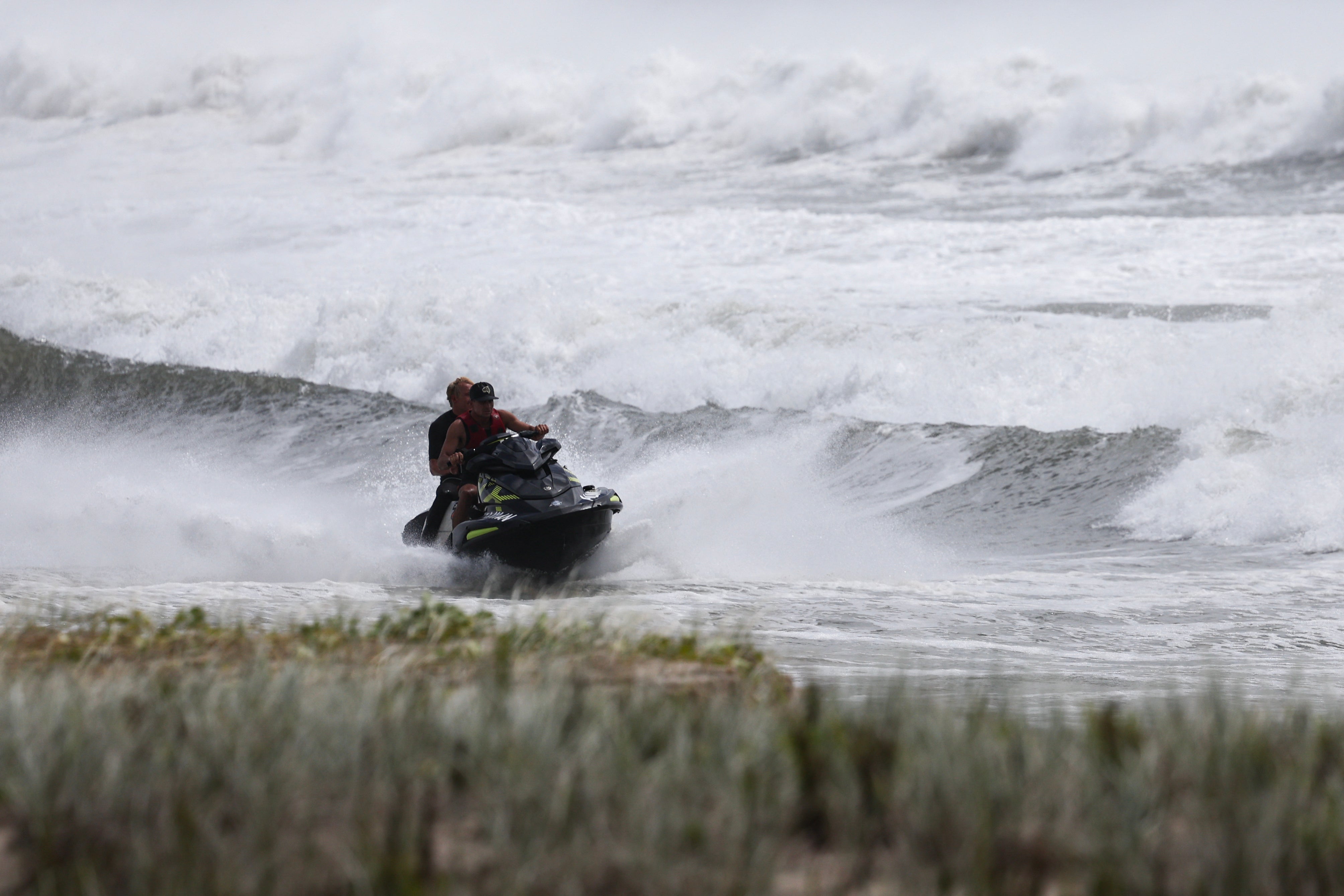 A jet ski with surfers move across record-breaking waves at Kirra Beach