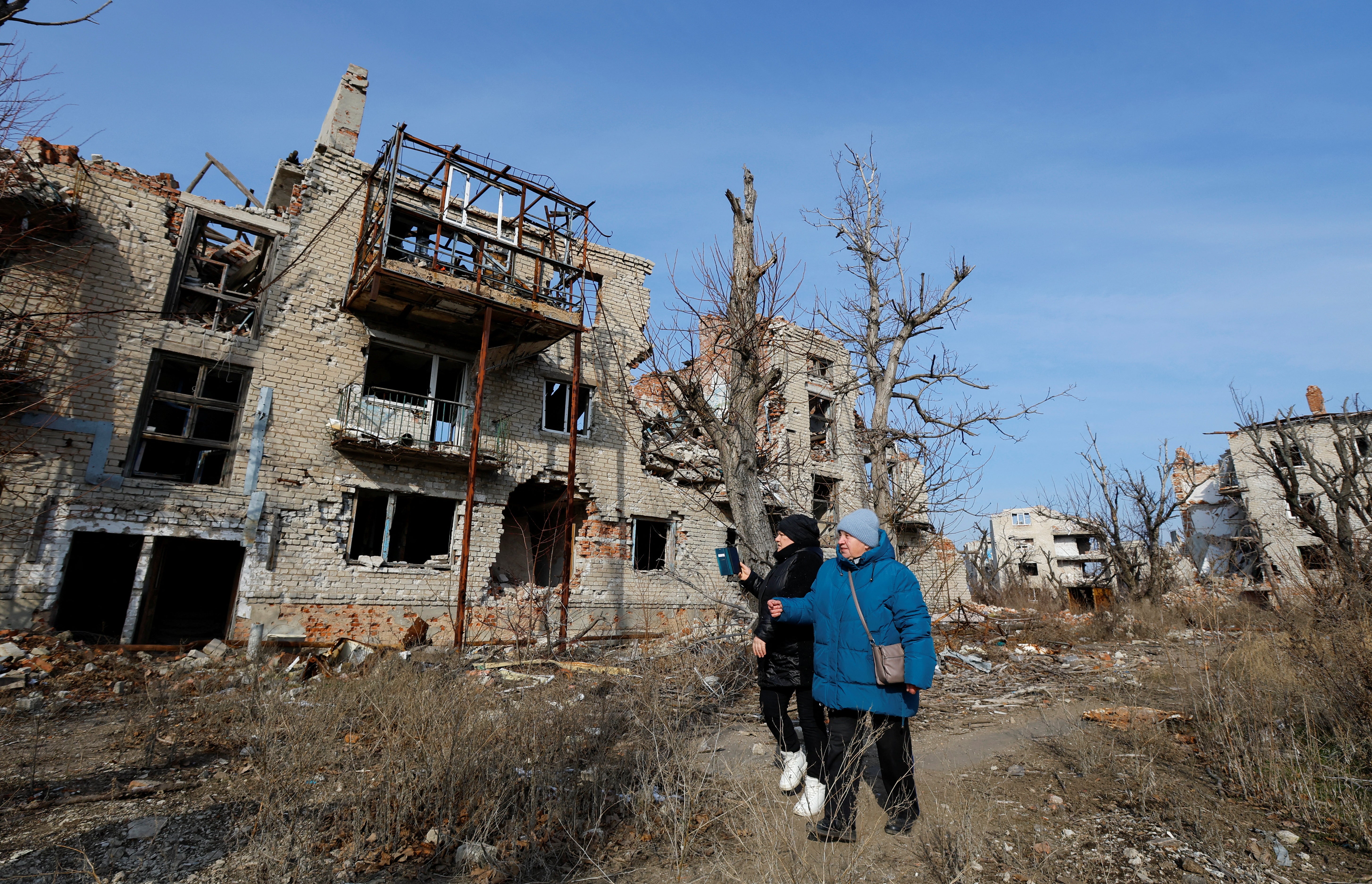 Residents Yekaterina Tkachenko, 75, and Maria Seryogova, 49, walk past ruins of buildings as they come to visit their apartments destroyed in Pisky, a Russian controlled region of Ukraine