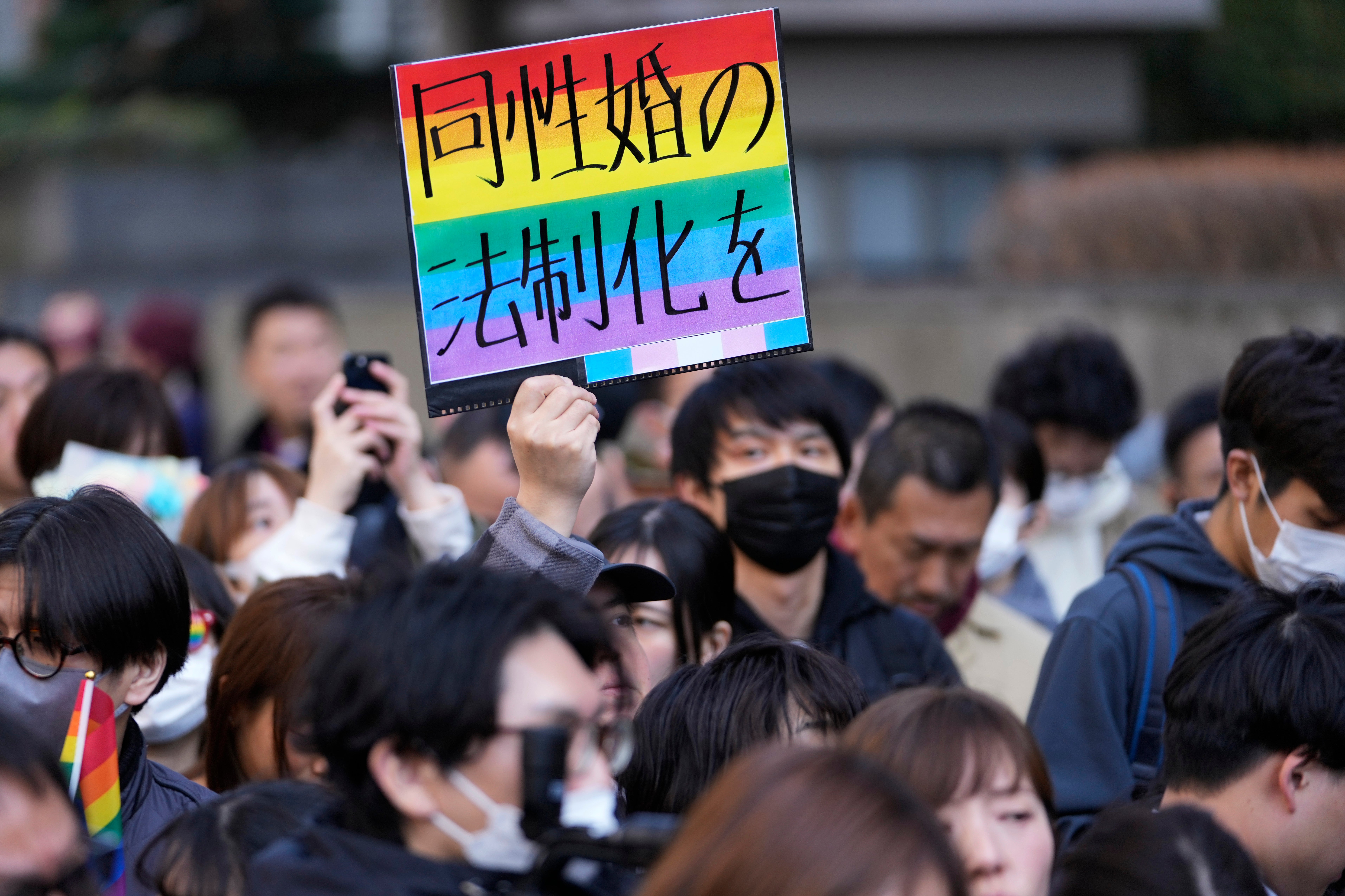 A supporter for the LGBTQ+ community holds up a poster reading ‘Legalize the same-sex marriage’ as plaintiffs speak in front of media members by the main entrance of the Tokyo district court after hearing the ruling regarding LGBTQ+ marriage rights