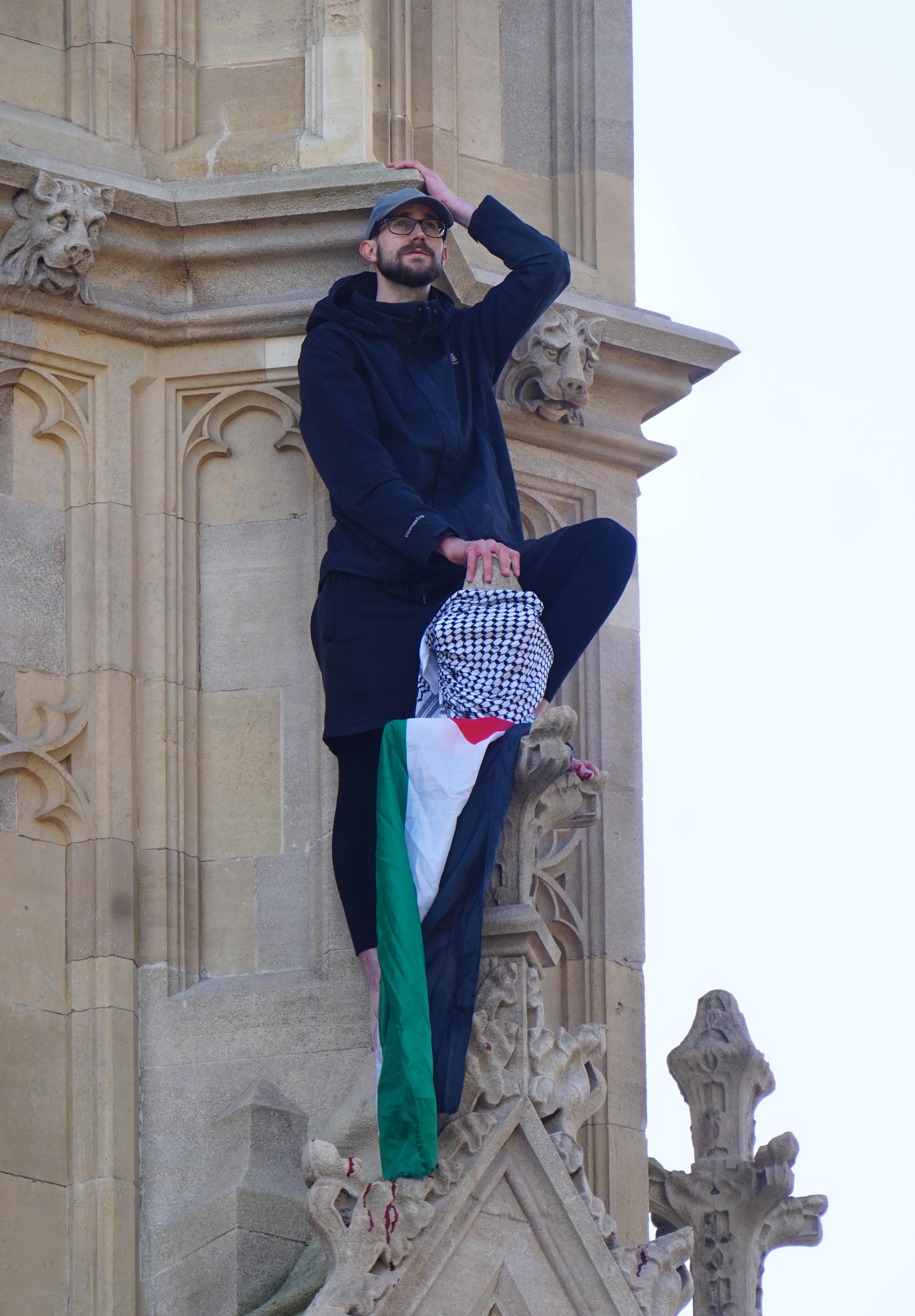 A barefoot man is seen standing on a ledge holding a Palestine flag several metres up Elizabeth Tower, which houses Big Ben