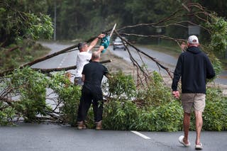 Residents remove branches of an uprooted tree across a road in the suburb of Currumbin