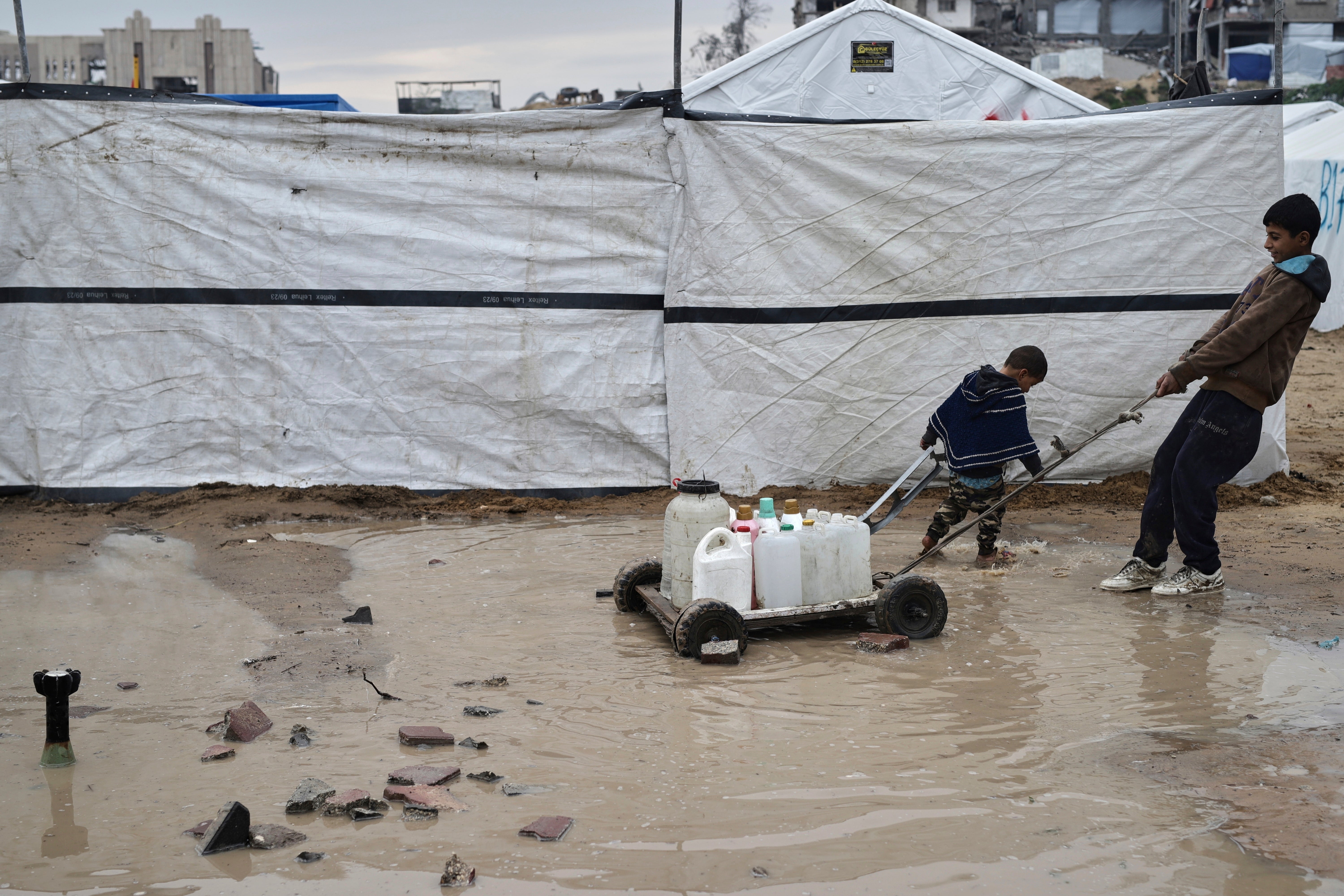 A small boy pulls containers full of fresh water on a trolley through the mud