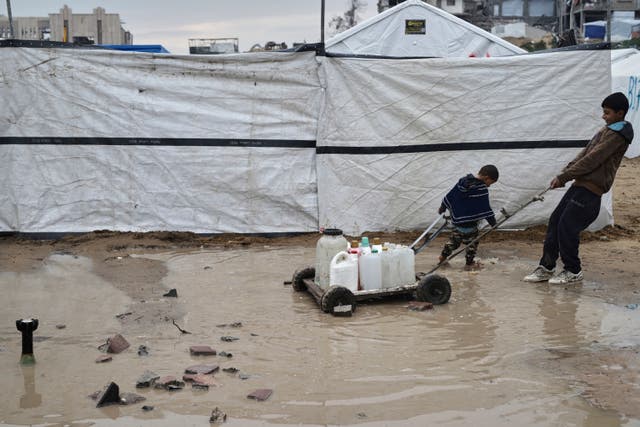 <p>A small boy pulls containers full of fresh water on a trolley through the mud</p>