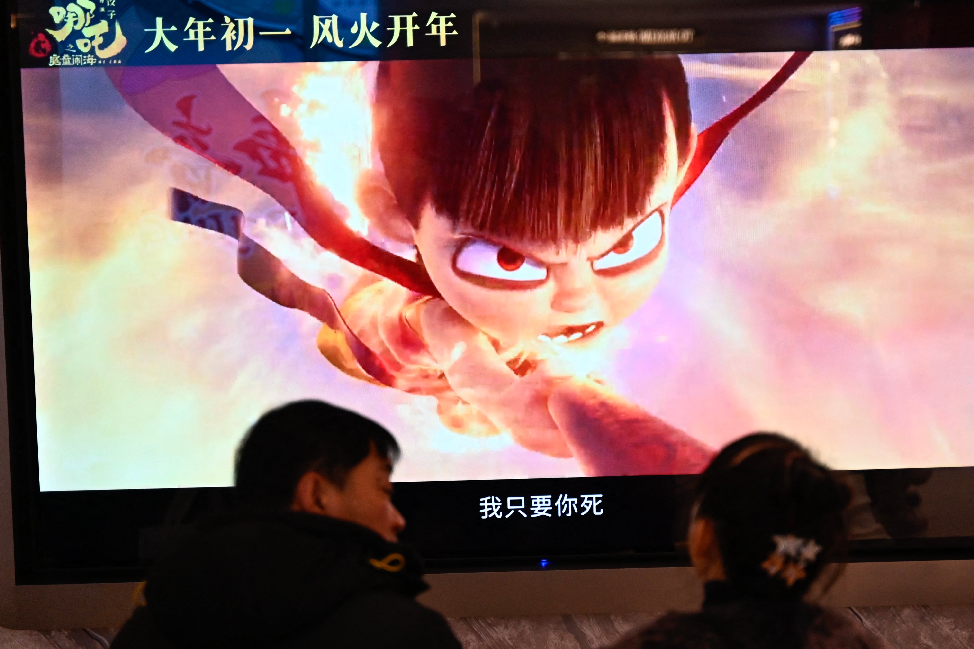 People wait as a screen displays a scene from the Ne Zha 2 animated film at a movie theatre in Beijing on February 16, 2025
