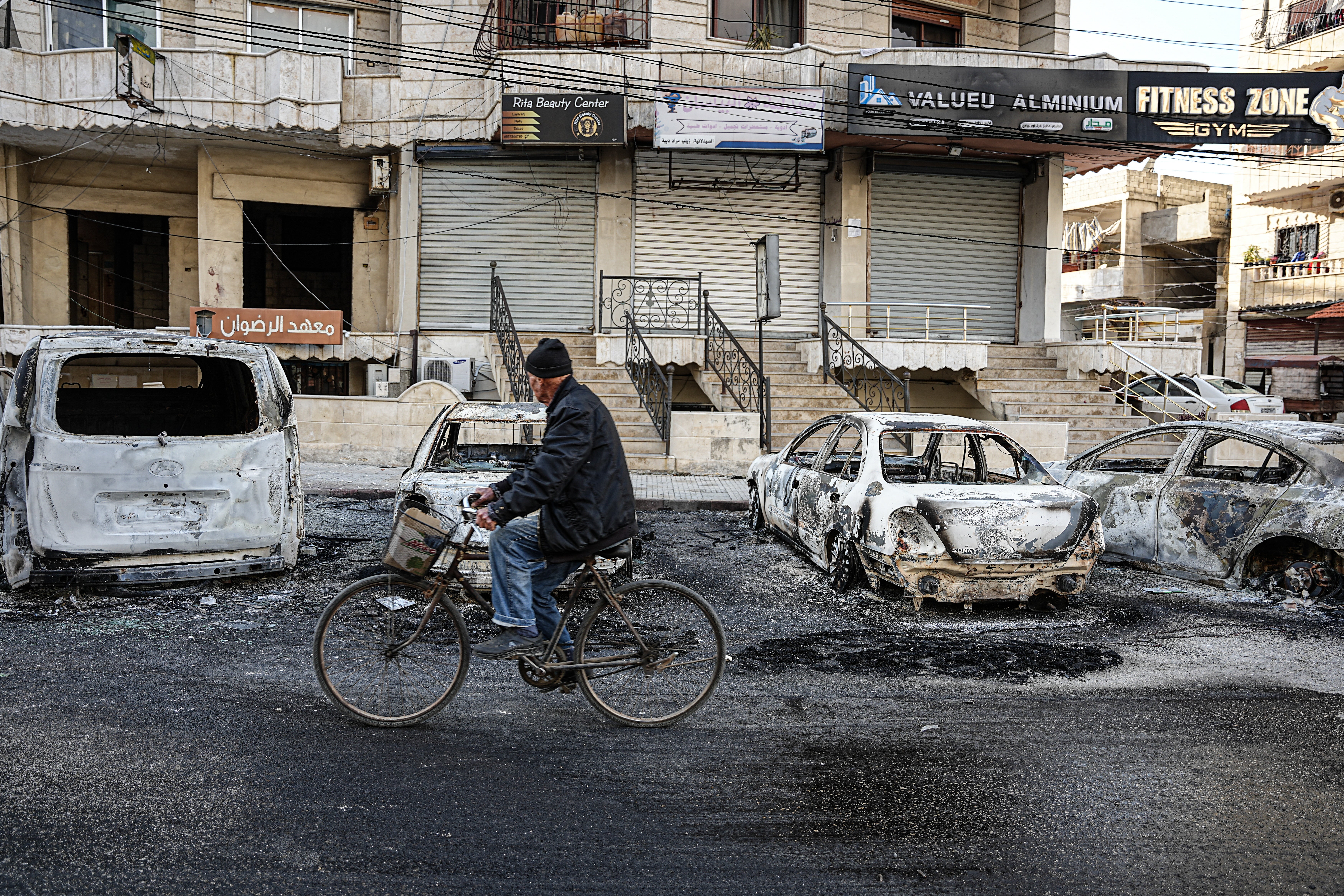 A Syrian man cycles past damaged cars in Latakia