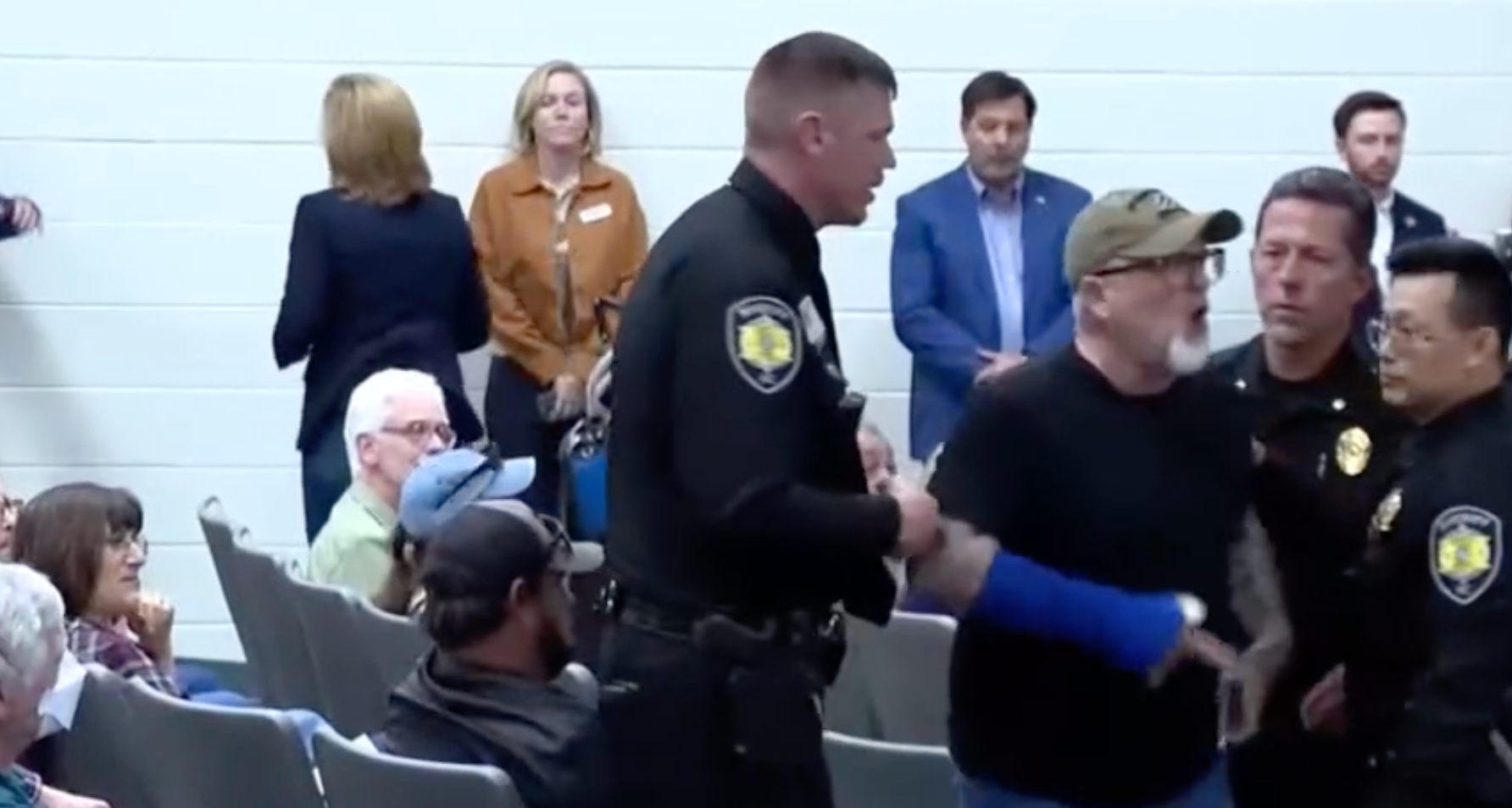 Officers lead out an angry constituent shouting at Representative Chuck Edwards's town hall Thursday