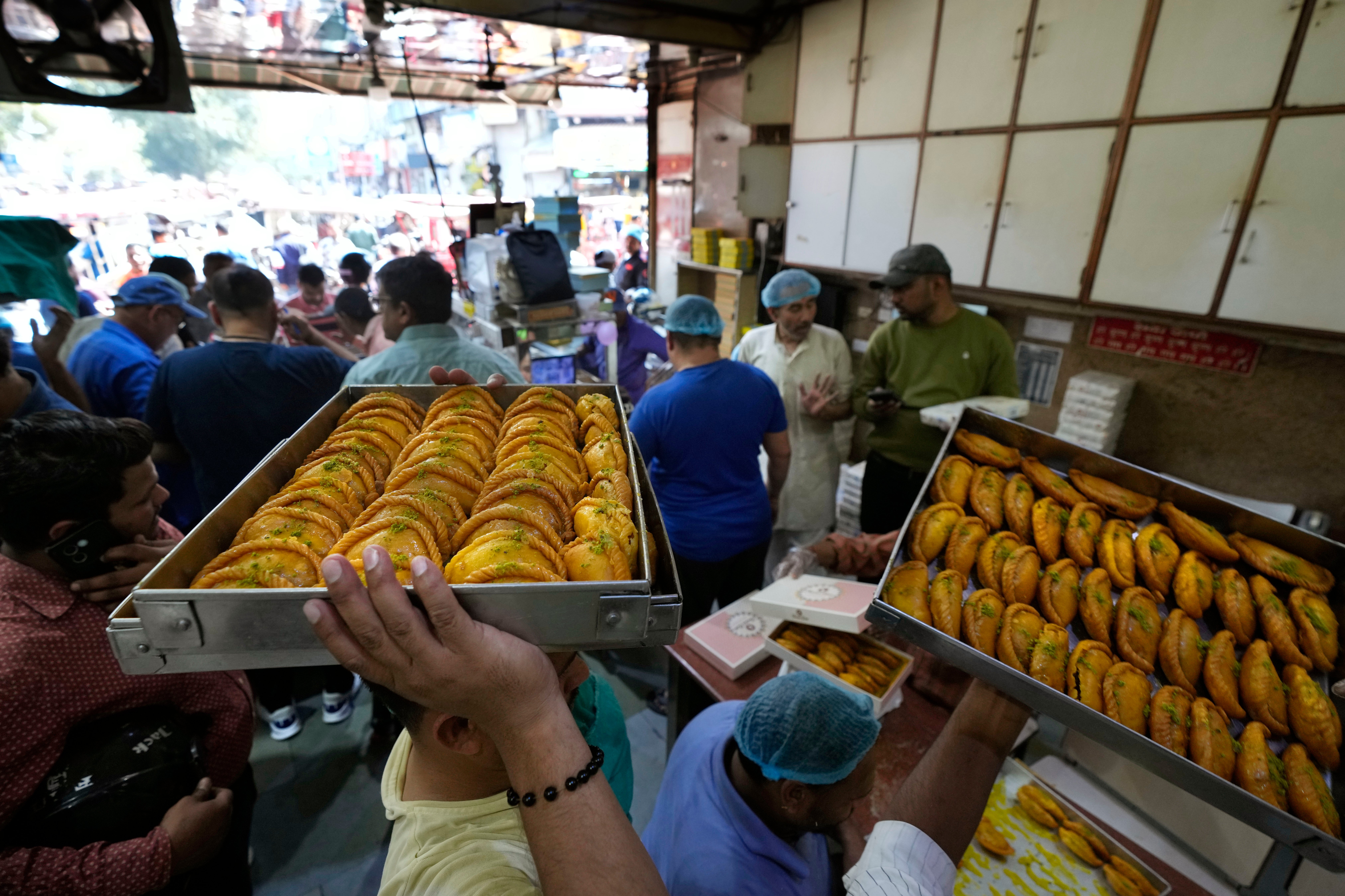 Staff carry Gujiya, a sweet dish that is specially made for Holi, at a sweet shop in the national capital Delhi