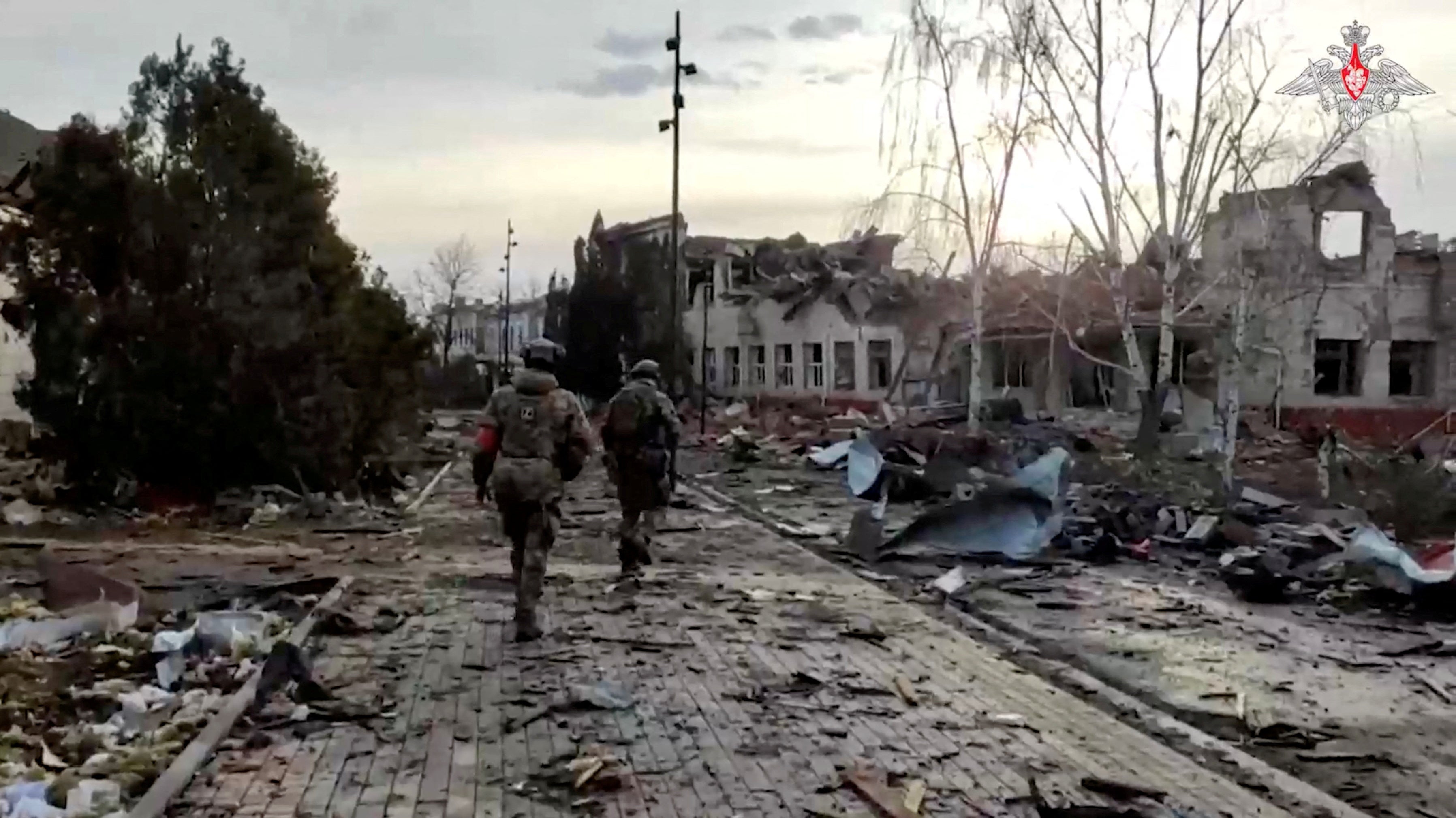 Russian service members walk past a destroyed building in the town of Sudzha