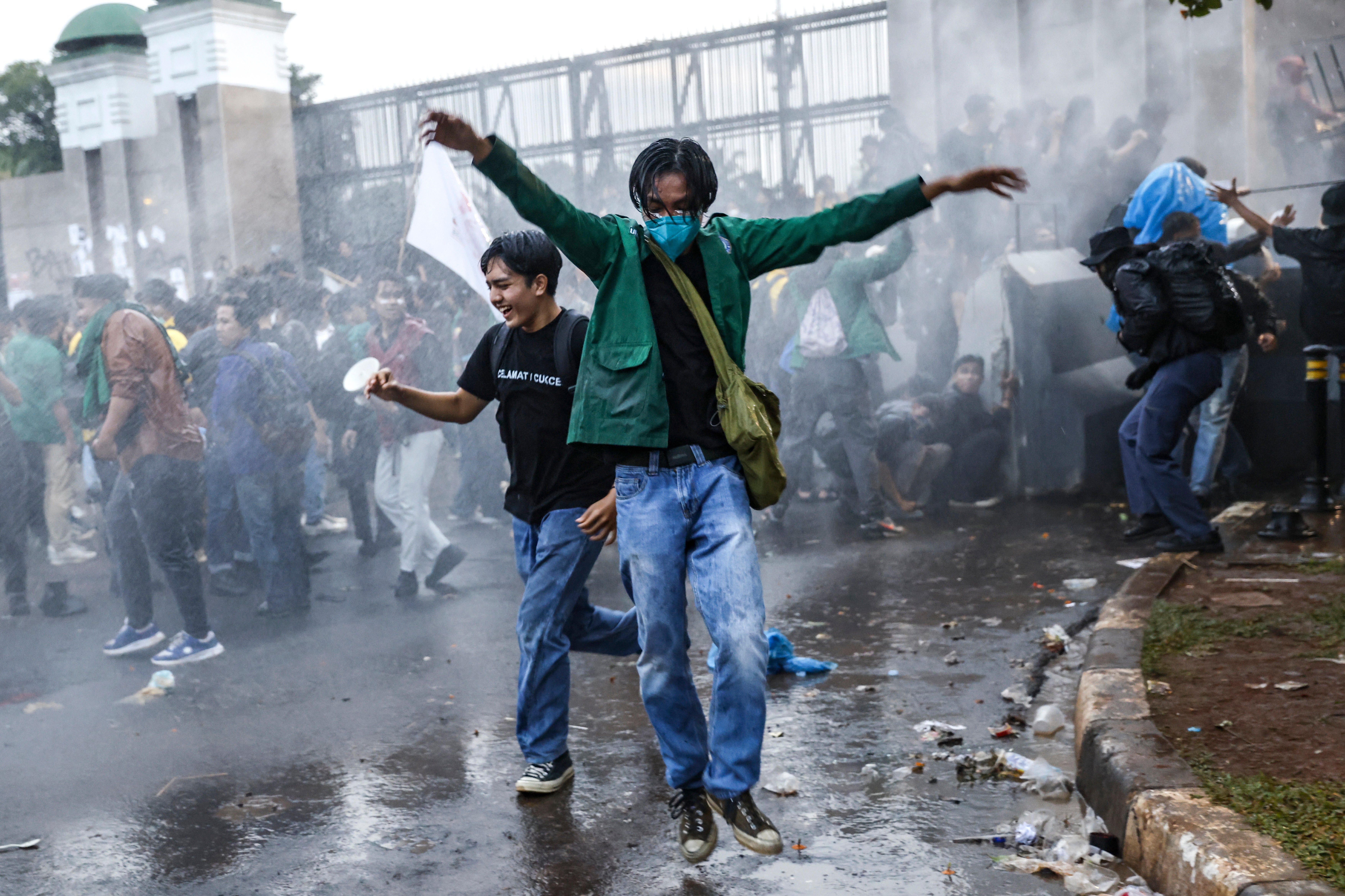 Protesters react as Indonesian police spray water to disperse them during a demonstration against the revision to the country's military law outside the parliament building in Jakarta