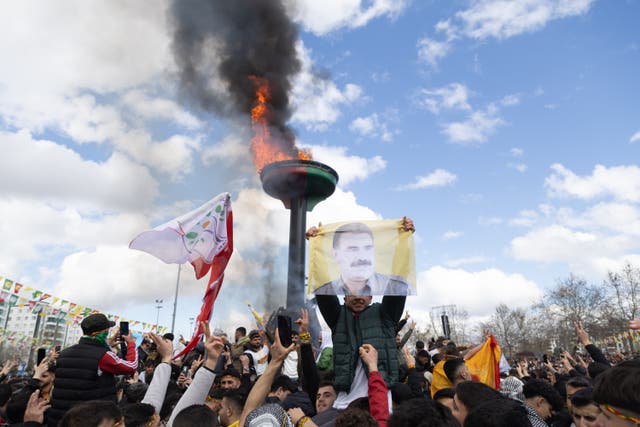 <p>Supporters of The Peoples' Equality and Democracy Party (DEM) hold pictures of Kurdistan Workers' Party (PKK) jailed leader Abdullah Ocalan, and shout slogans next to a bonfire during a rally for Newruz celebrations in Diyarbakir, Turkey, 21 March 2025</p>