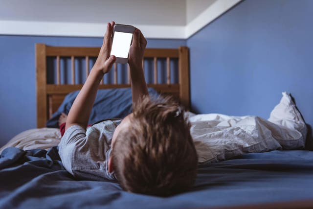 A child looks at a phone screen in his bedroom (Alamy/PA)
