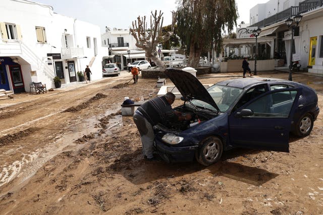 <p>A man tries to fix a car which was inundated in flooding on Paros</p>