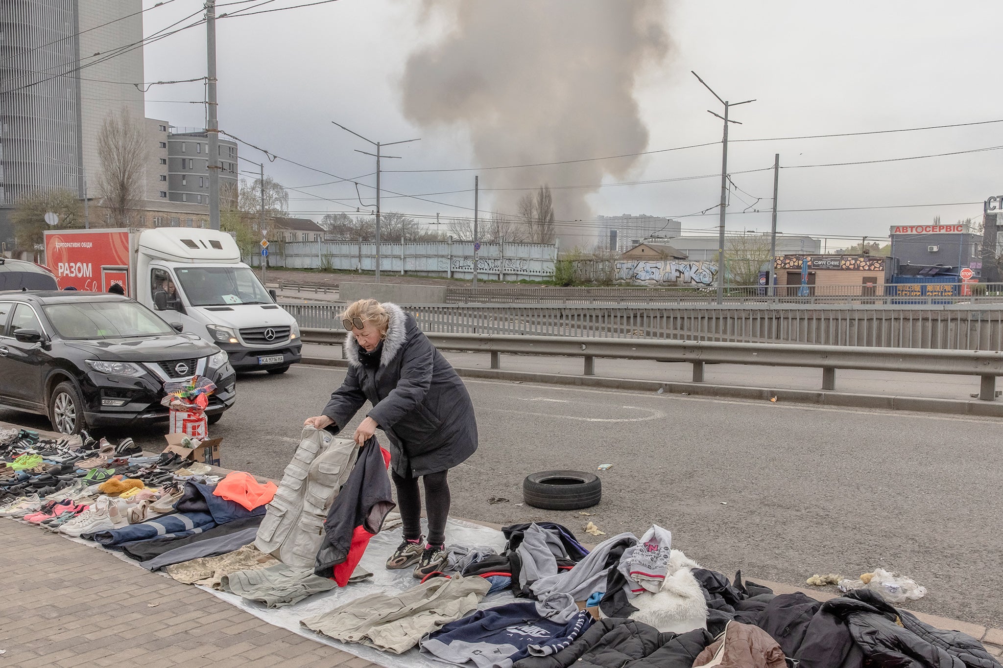 A street vendor prepares items for sale at a flea market as smoke rises in the distance following a Russian missile attack, in Kyiv on April 6