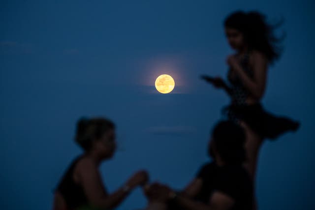 <p>A Super Pink Full Moon lights up the sky as people relax on the beach in Miami Beach on April 26, 2021. </p>