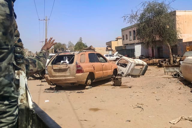 <p>A Sudanese army soldier gestures from the back of a vehicle as it drives past damaged cars lying along a street in Khartoum</p>