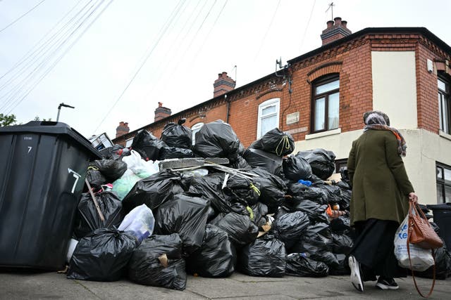 <p>A resident walks past uncollected bin bags piled up on Poplar Road in Birmingham</p>
