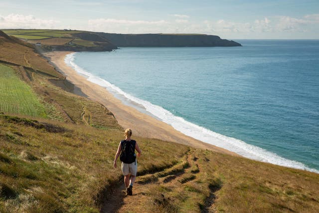 A woman strolls along the South West Coast Path above Porthleven Sands in Cornwall, England (Alamy/PA)