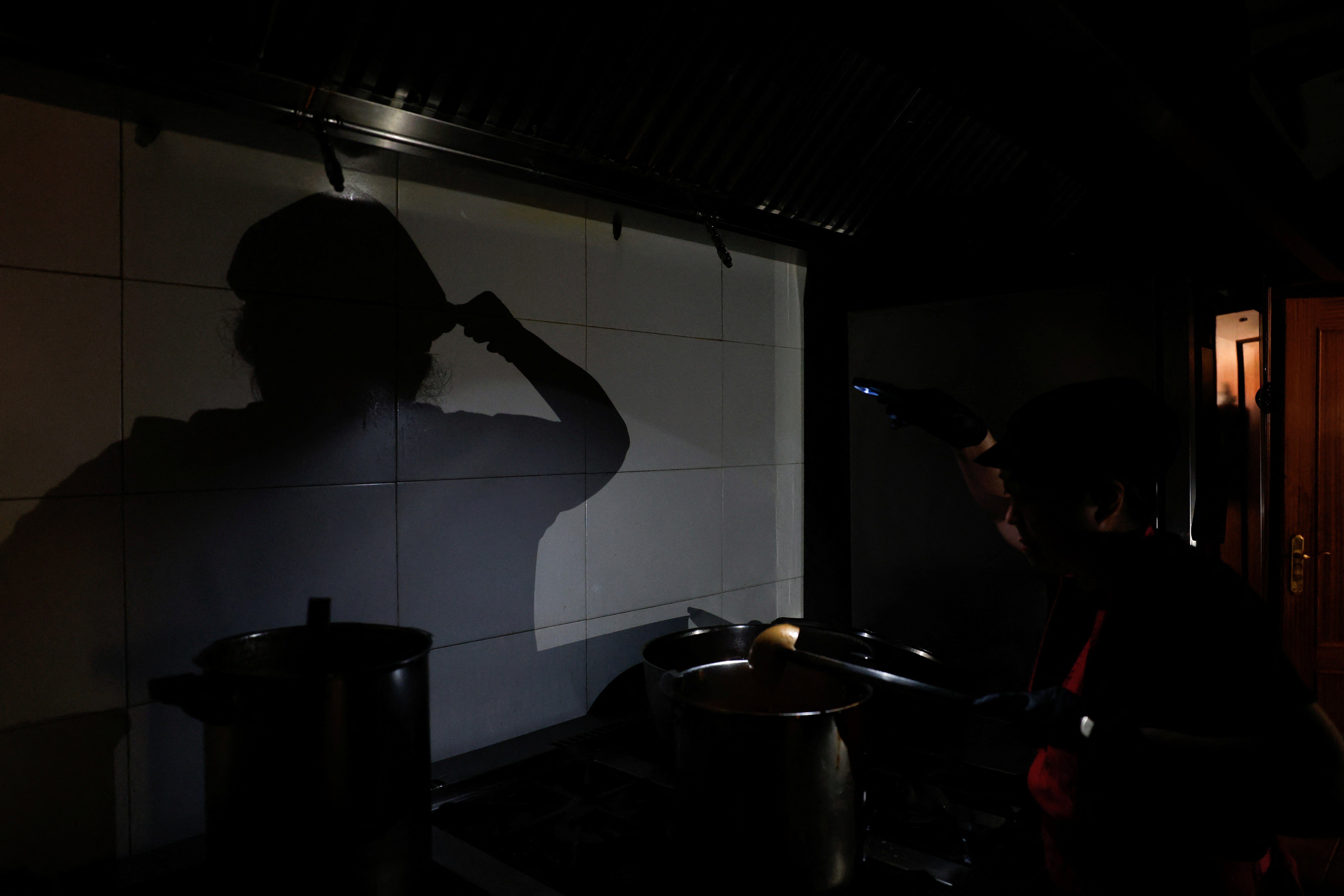 Un cocinero del restaurante de comida casera para llevar "La Cocinona" trabaja en una cocina oscura con la ayuda de la linterna de su teléfono durante un apagón en Madrid, España, el 28 de abril de 2025. REUTERS/Susana Vera