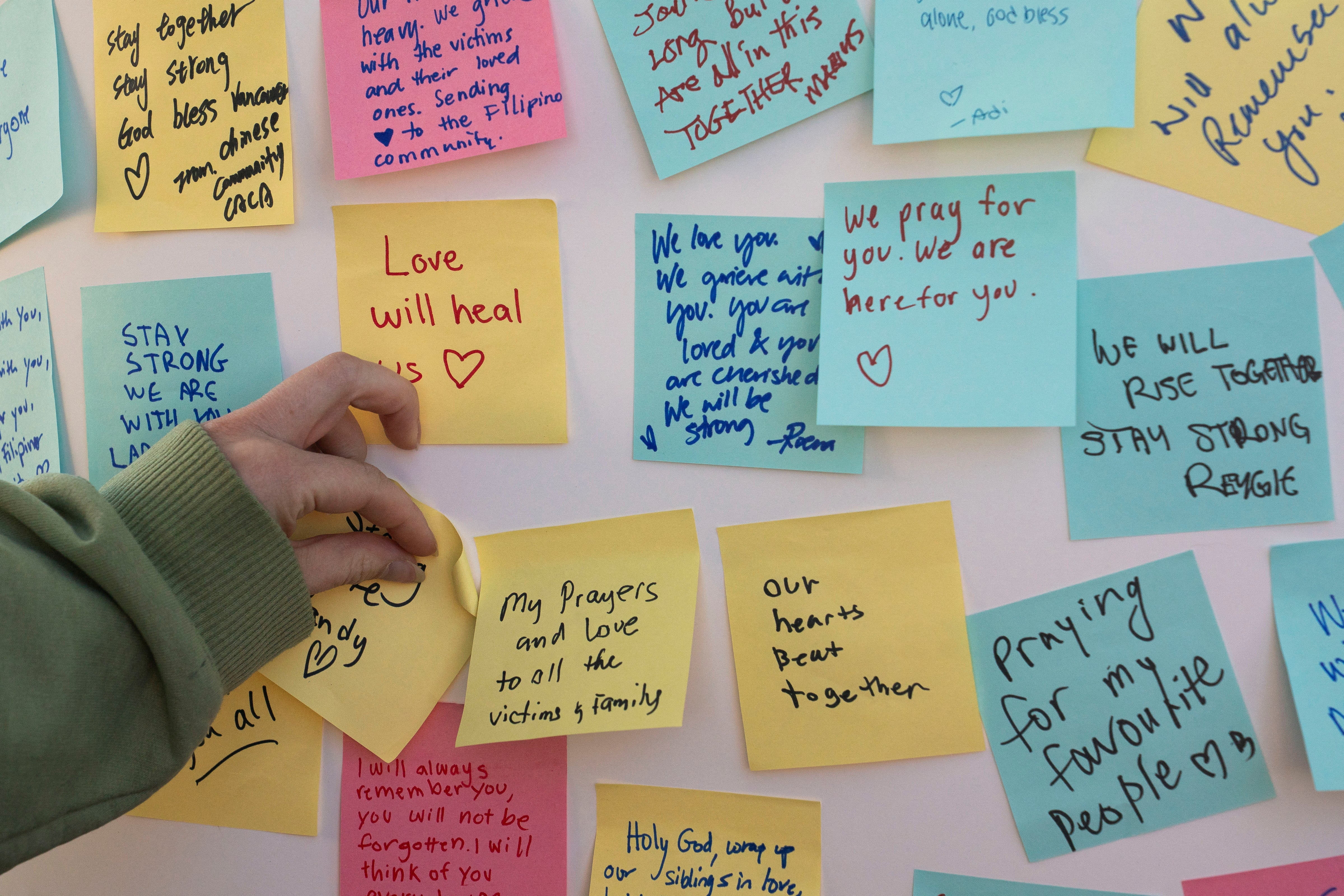 An attendee adds a handwritten note to a collection of others as community members gather at Kensington Park to mourn the day after a vehicle was driven into a crowd during Lapu Lapu day block party