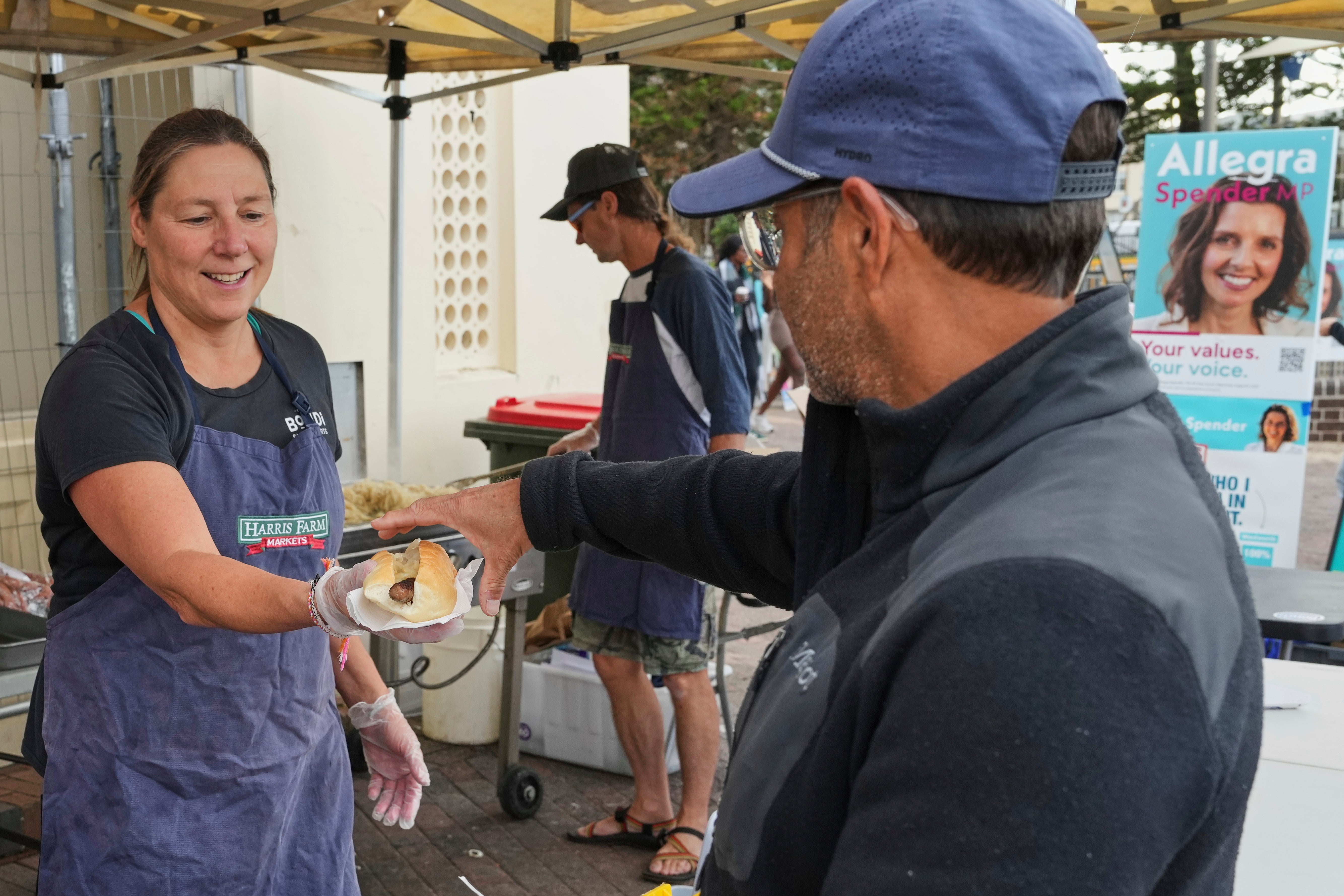 A volunteer hands a customer a sausage in a bread roll outside a polling booth at Sydney's Bondi Beach