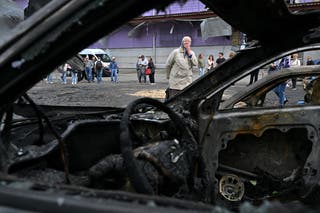 An elderly woman reacts as she looks at burned cars parked outside a mall following a night-time drone attack on Kyiv, on May 4