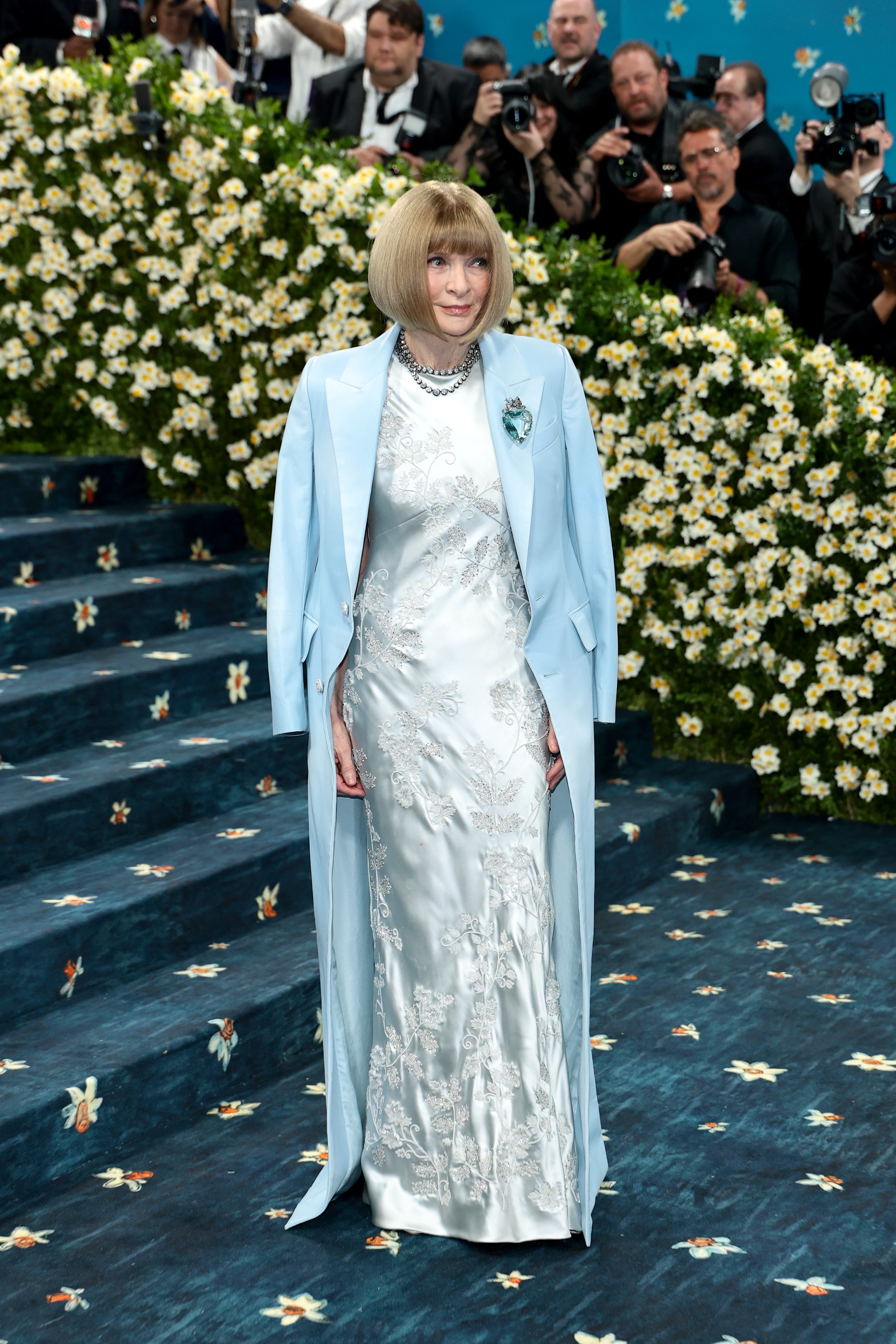 Vogue Editor-in-Chief Anna Wintour chose not to stray from her usual silhouette for the 2025 Met Gala, wearing a baby blue Tuxedo-style jacket over a white satin floor-length gown with floral embroidery