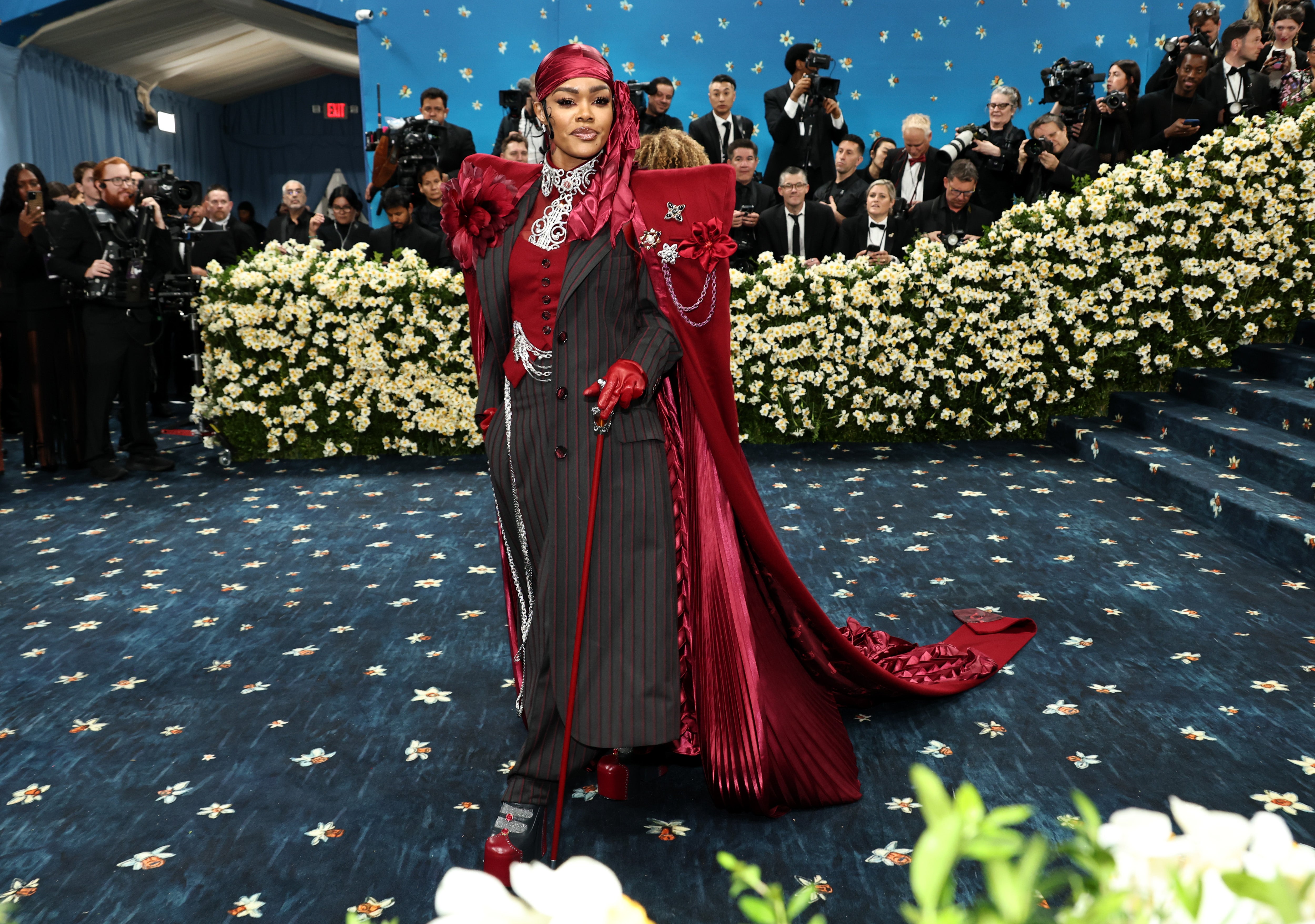 Teyana Taylor, one of ‘Vogue’s’ red carpet livestream hosts, stepped out on the Met Gala red carpet in a custom ensemble comprised of a black pinstripe suit, maroon red top hat, and a matching cape inscribed with ‘Harlem Rose’