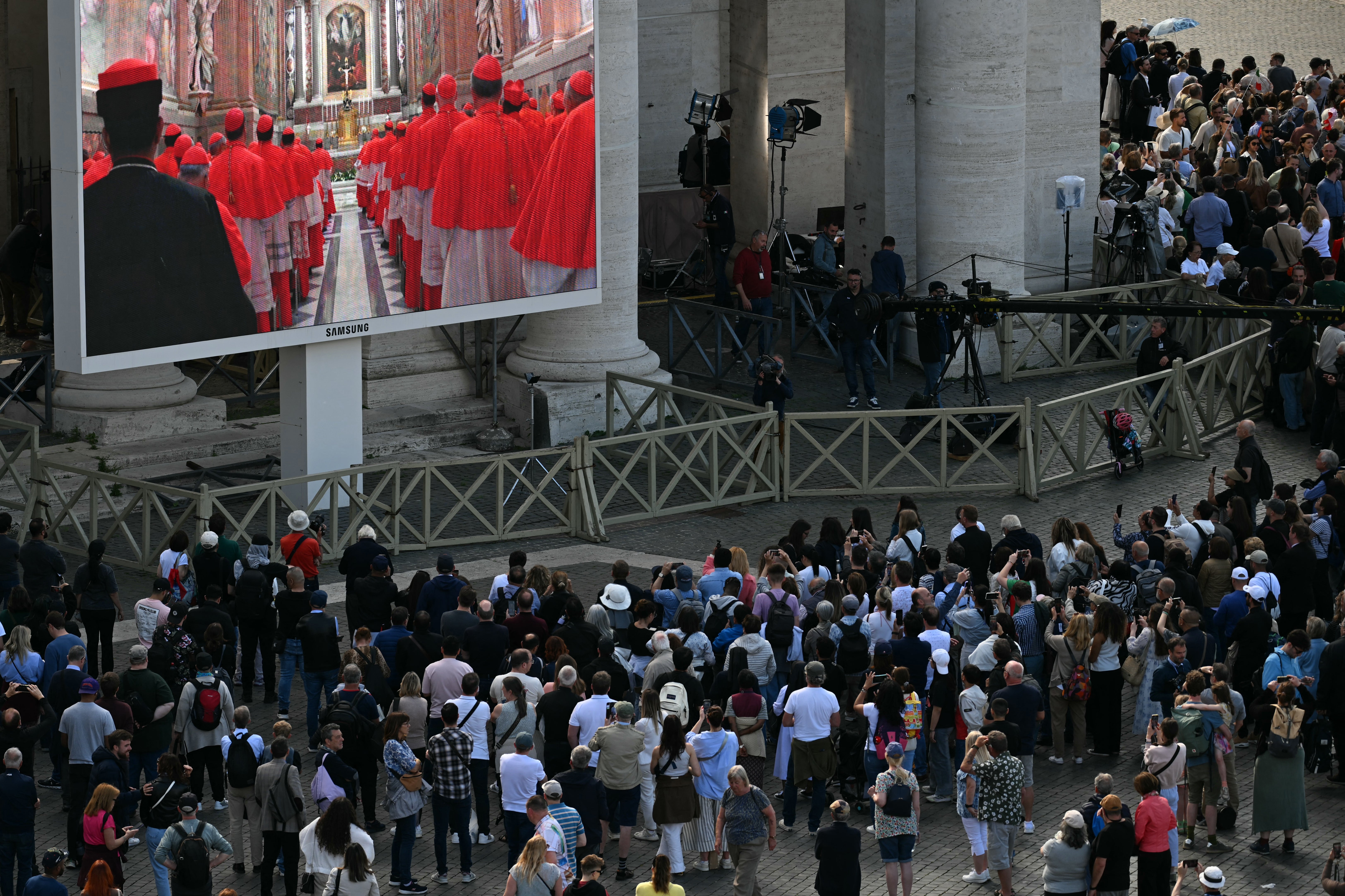 Visitors watch the cardinal's procession to the Sistine Chapel displayed on a screen in St Peter's Square