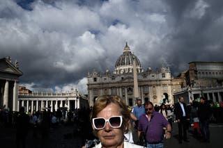 Pedestrians walk near the Vatican with the St Peter's basilica in the background