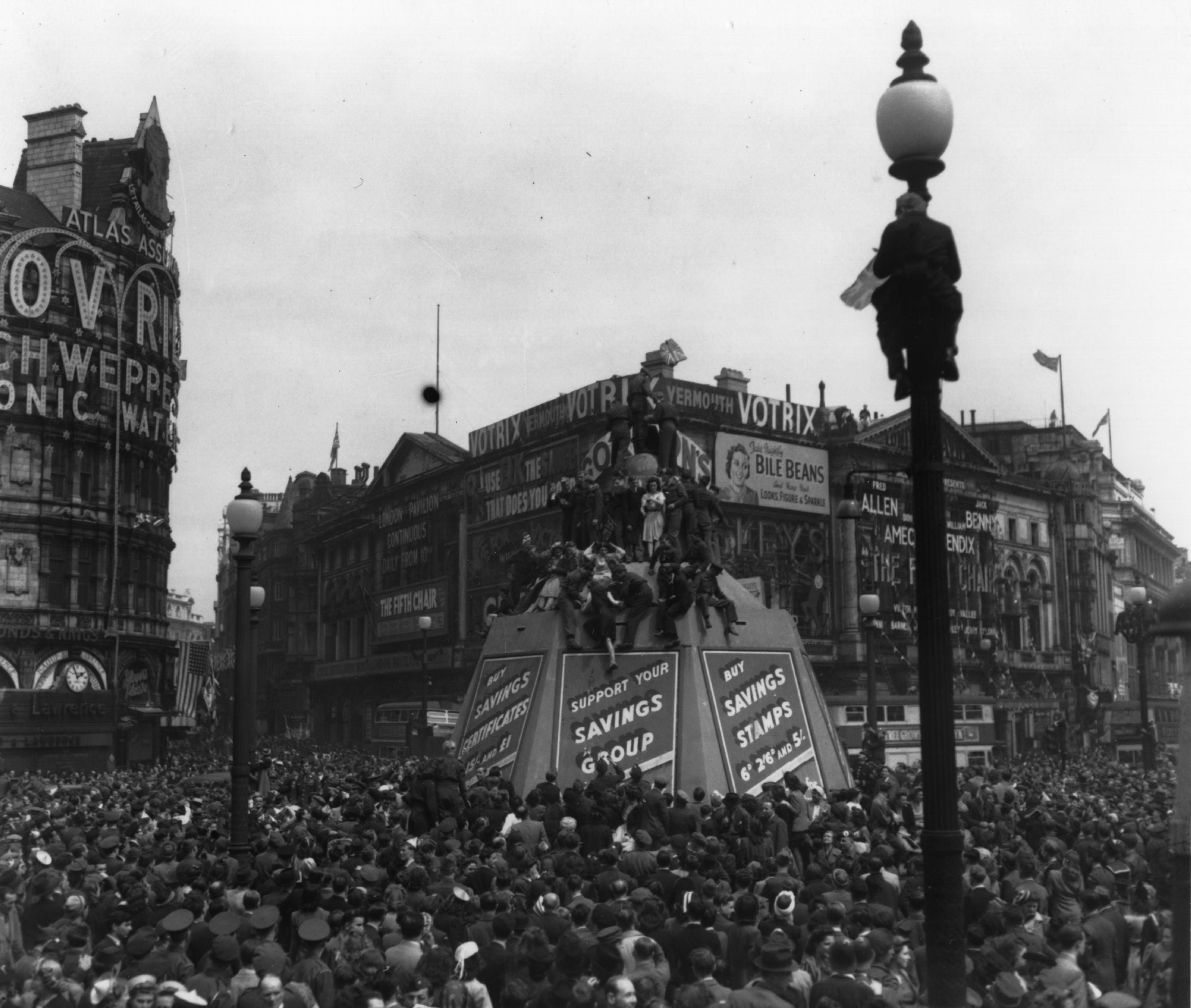 Crowds in Piccadilly Circus climb lampposts and the Eros statue's protective container, on VE Day.