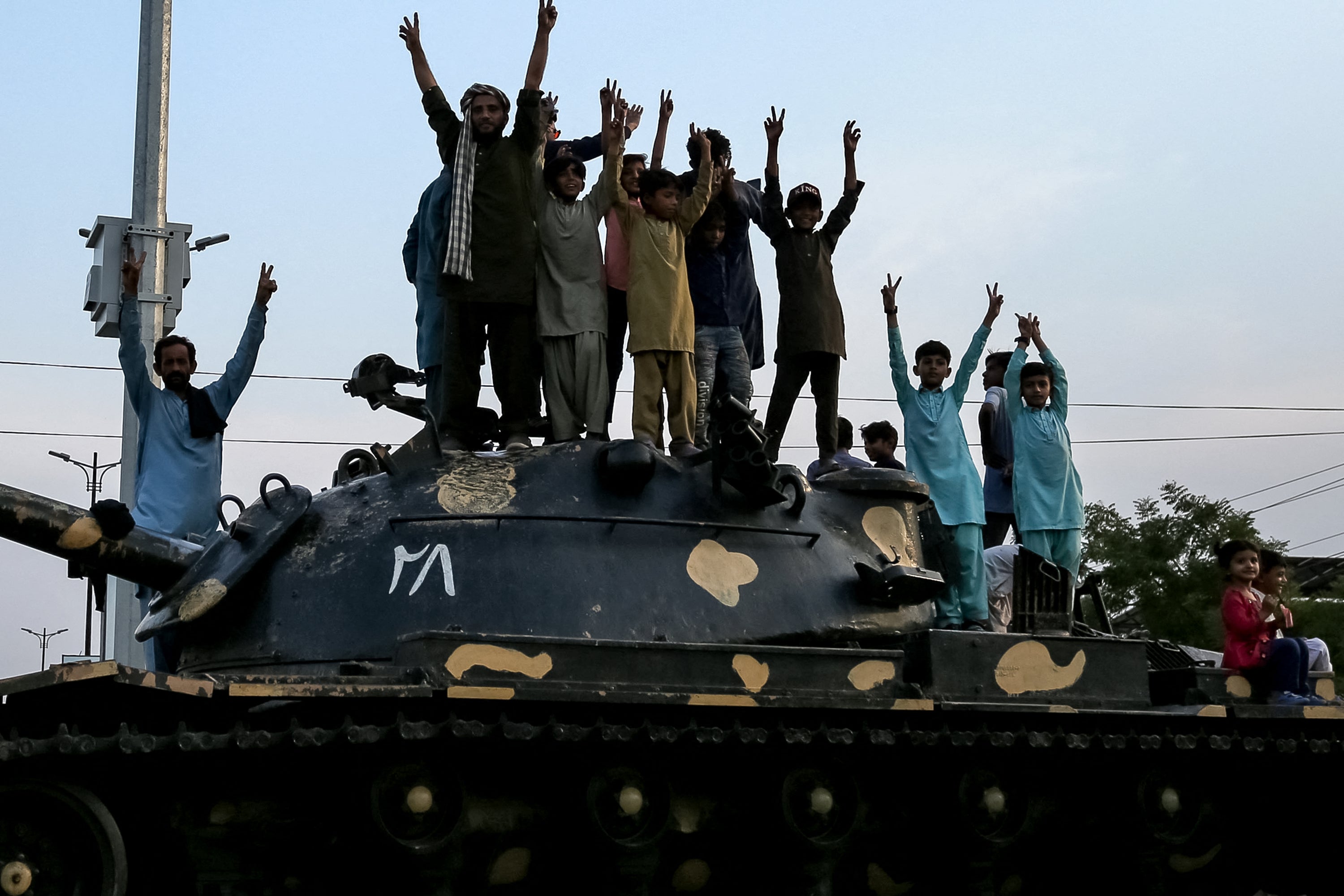 Pakistani people flashing victory signs stand over a tank as they celebrate after the ceasefire