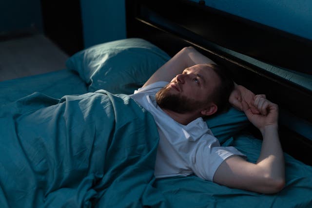 Stressed man feels from insomnia trying to sleep in his bed at night