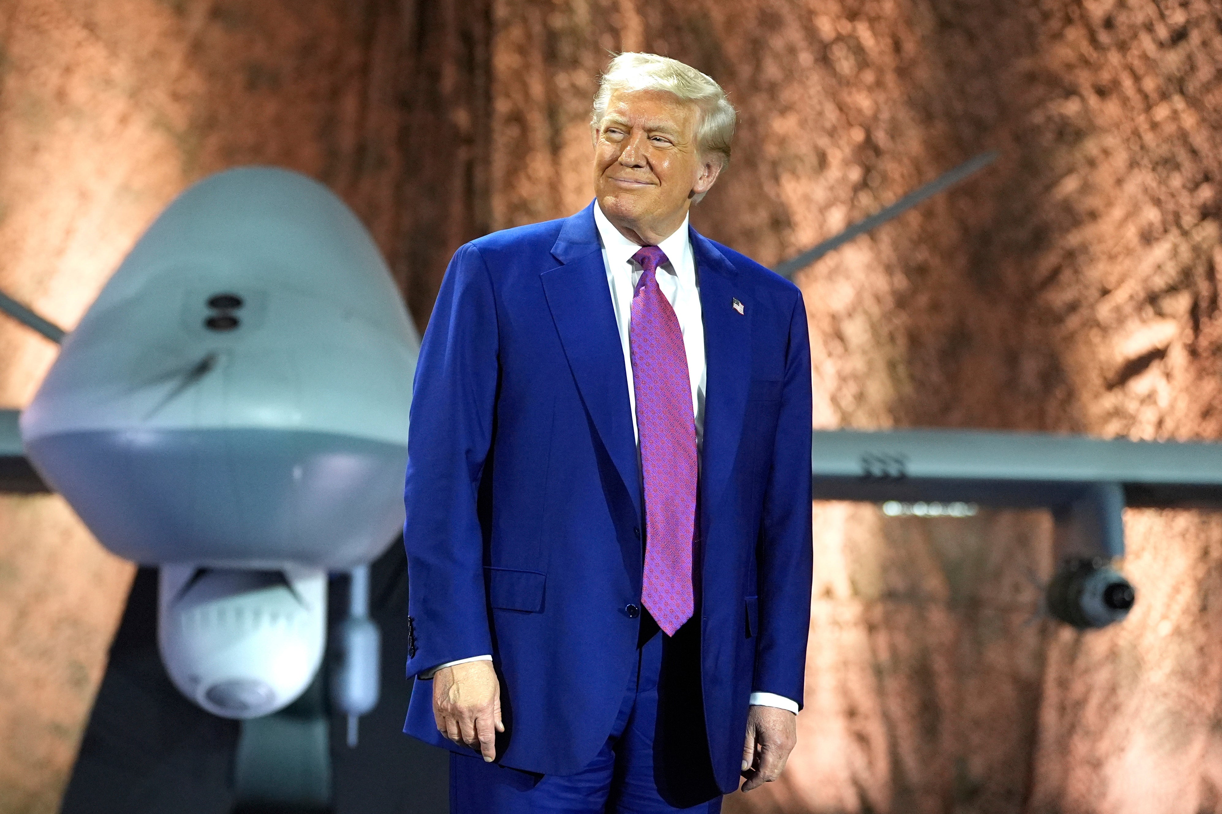 President Donald Trump smiles backdropped by an MQ-9 Reaper drone before addressing military personnel at the Al Udeid Air Base, Thursday, May 15, 2025, in Doha, Qatar. (AP Photo/Alex Brandon)