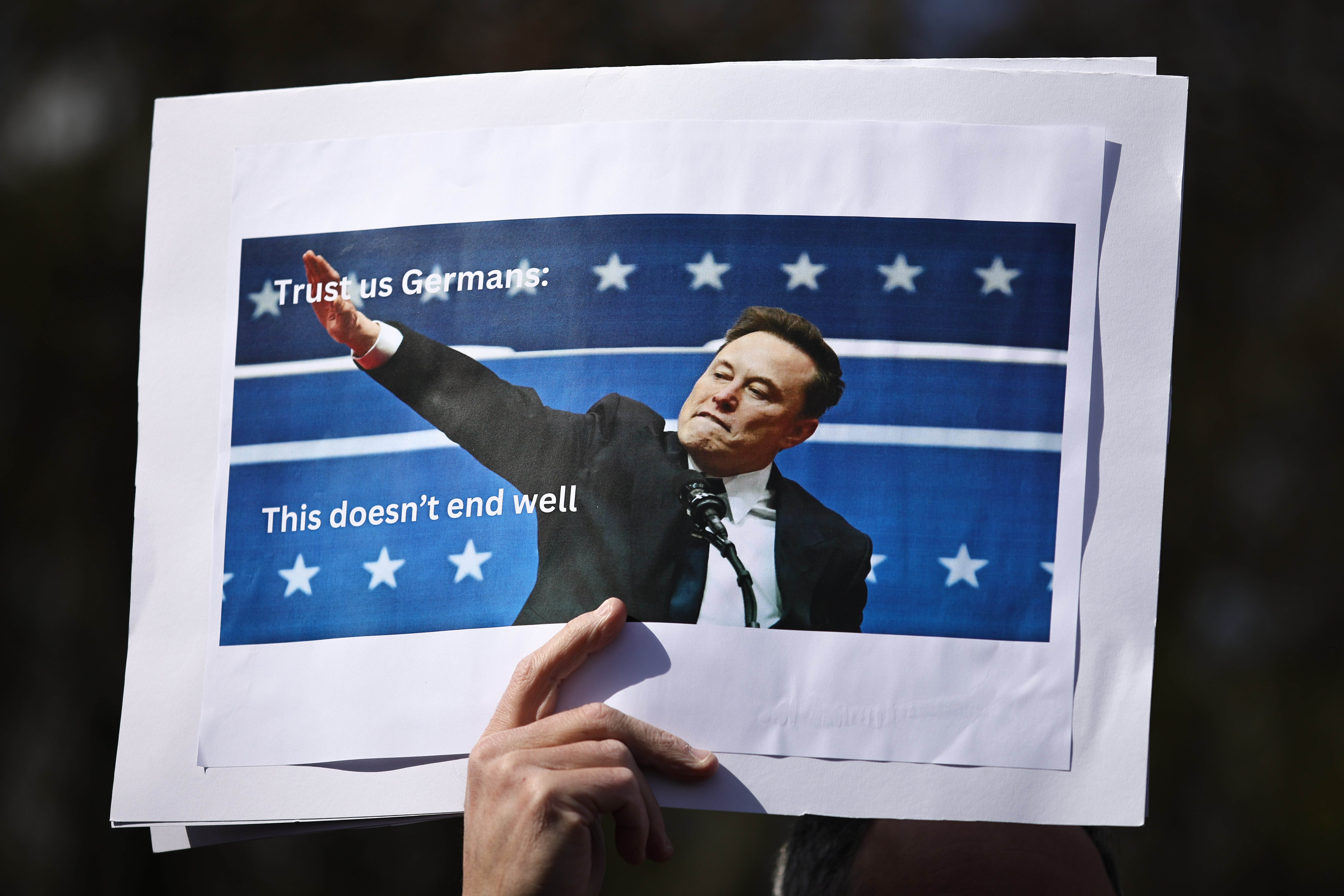 A demonstrator holds a photo of Elon Musk with his arm raised similarly to a ‘Nazi salute’