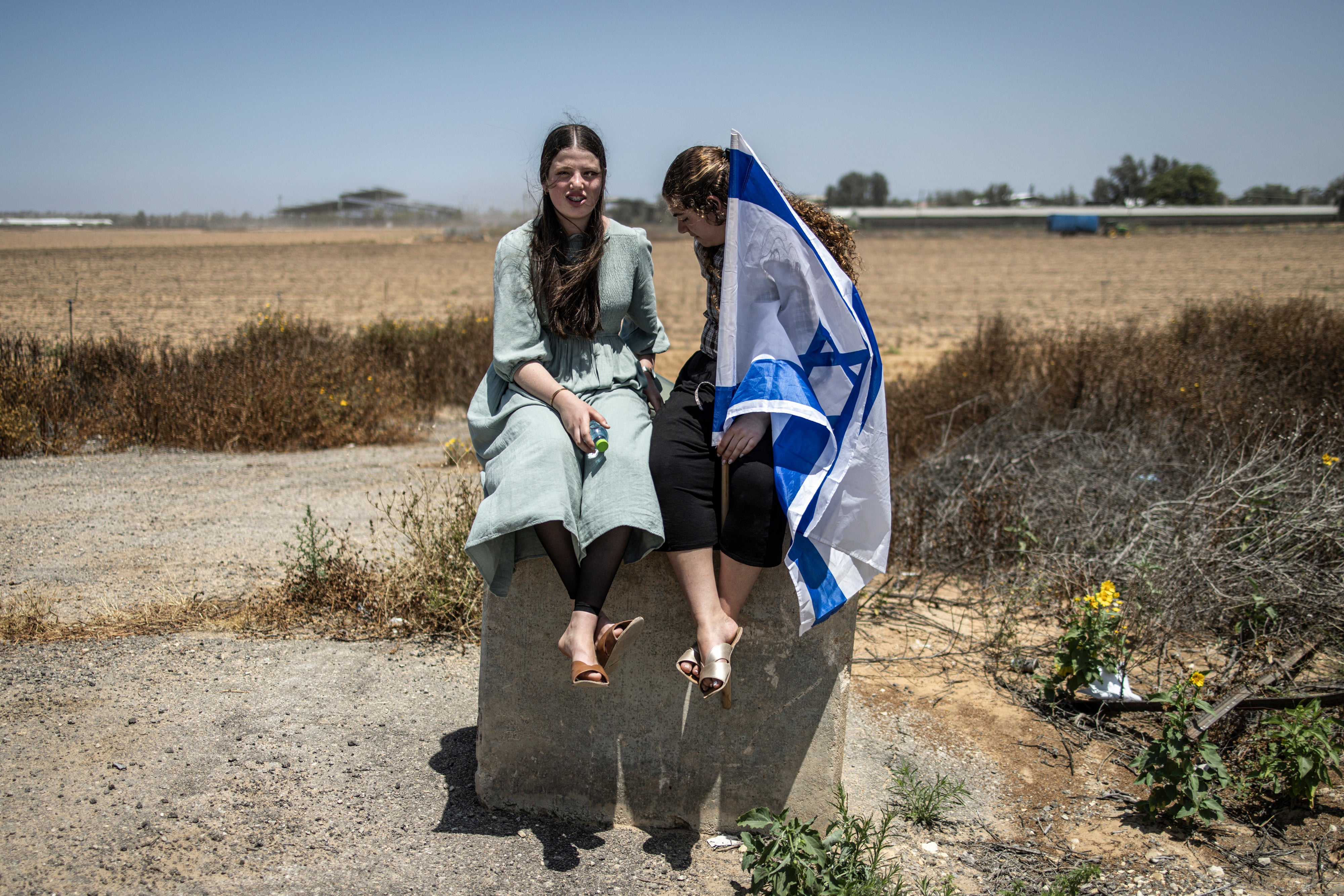 Israeli women sit on a concrete block holding their national flag as right-wing demonstrators gather in an attempt to block humanitarian aid from entering Gaza