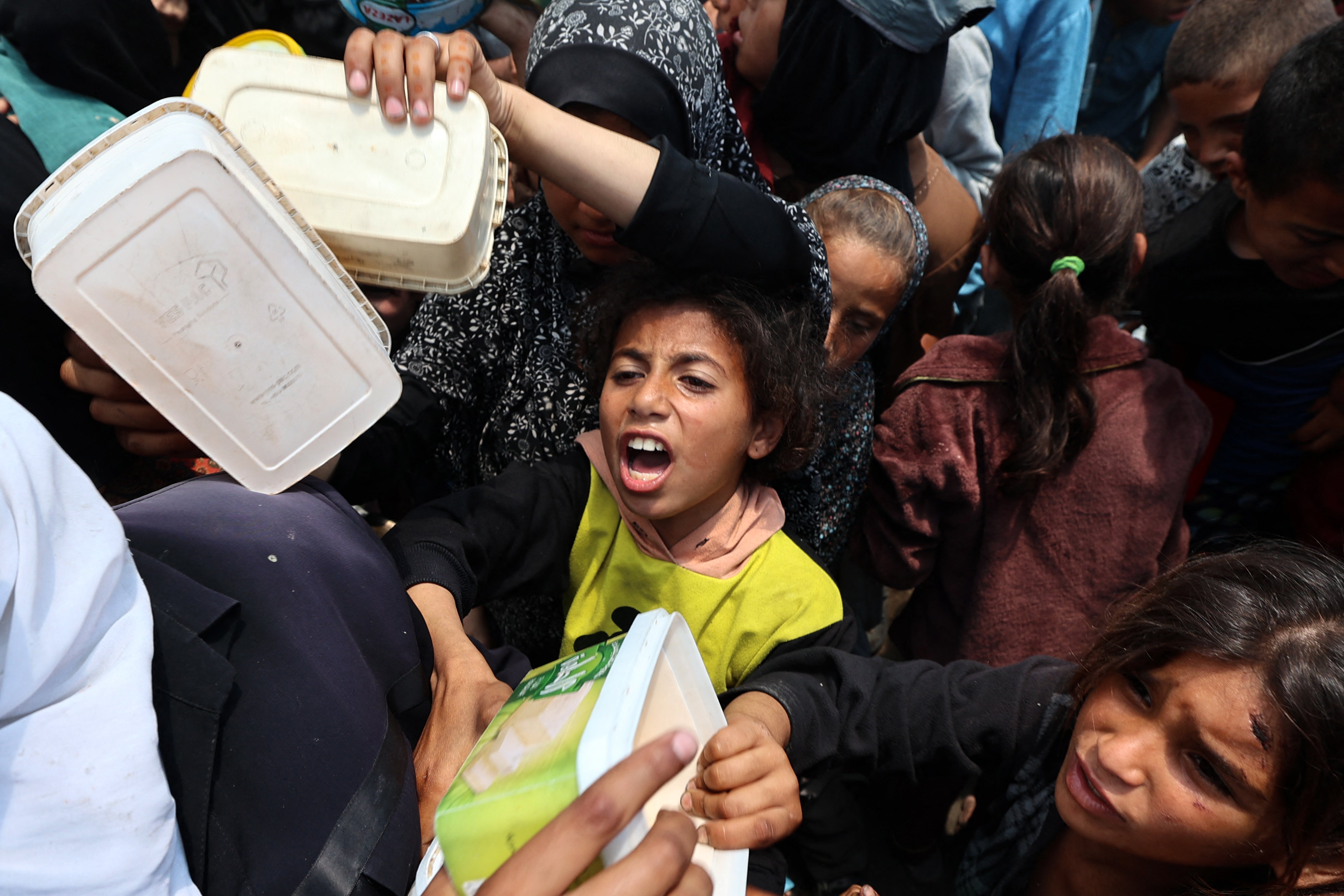 A Palestinian girl reacts as people gather for a hot meal at a food distribution point