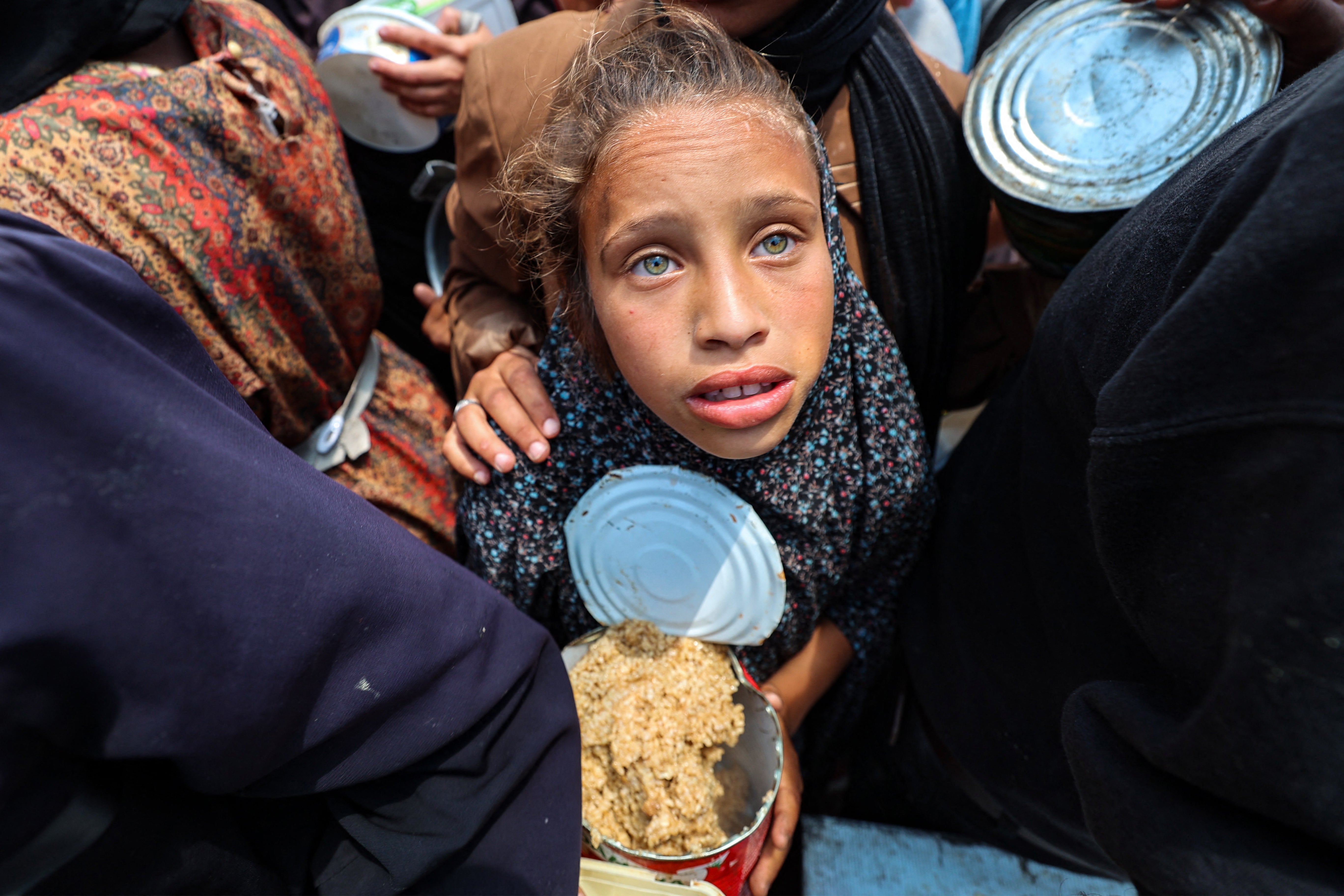 A Palestinian girl holds a container at a food distribution point in the Nuseirat camp for refugees