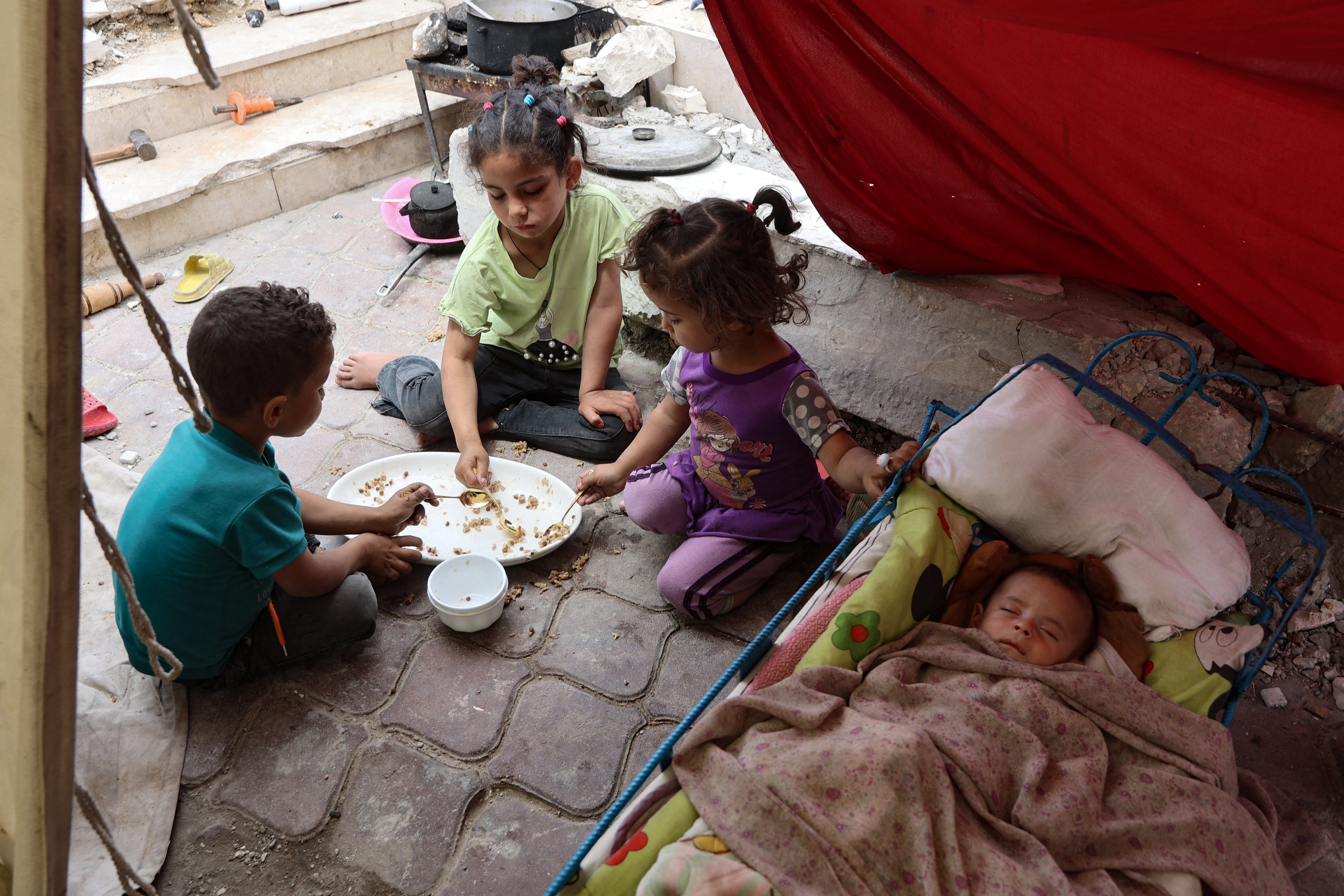 Palestinian children share a meal of rice as a baby sleeps, inside a tent at a displacement camp near Gaza City's port on Thursday