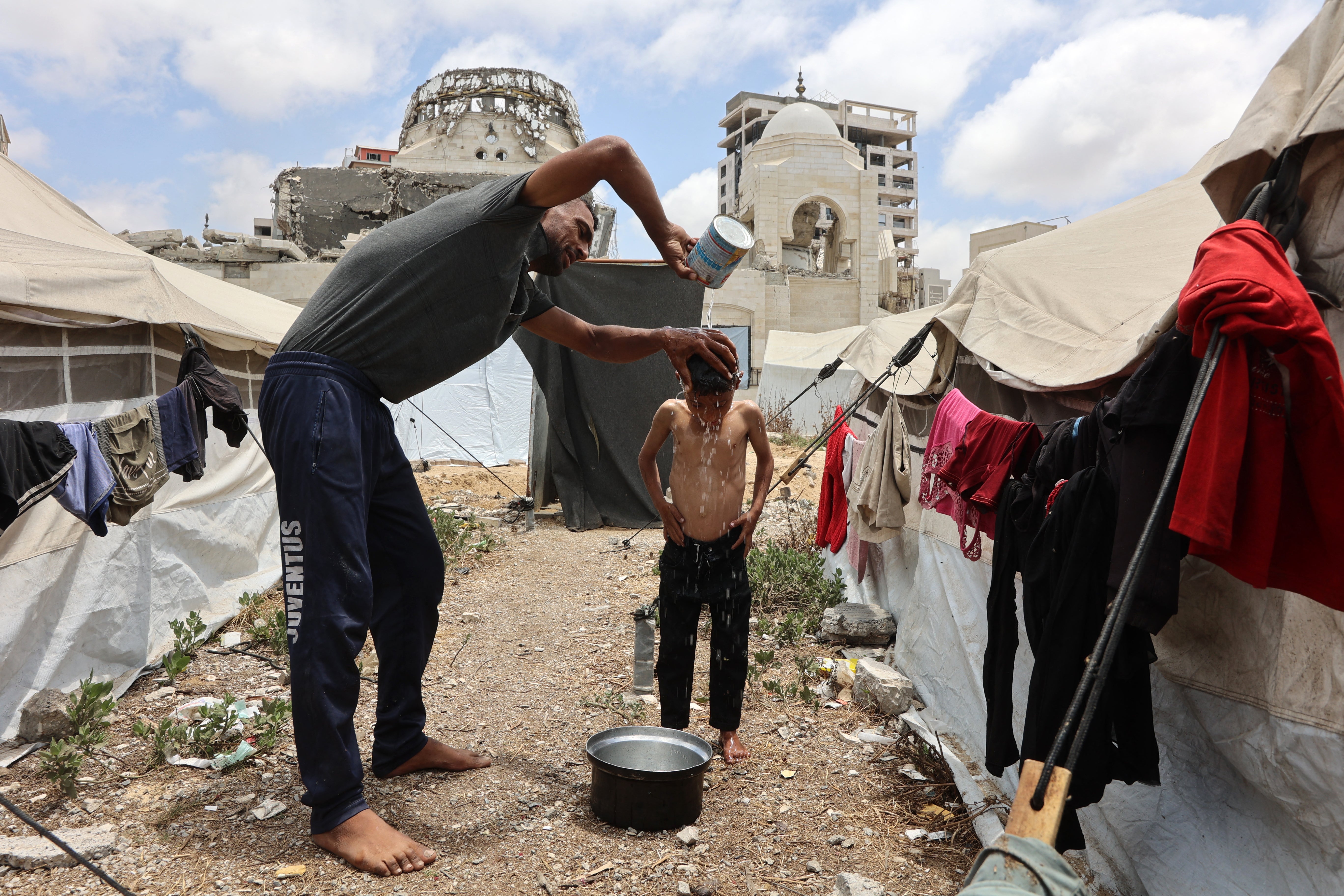 A Palestinian man washes a young boy, between tents at a displacement camp