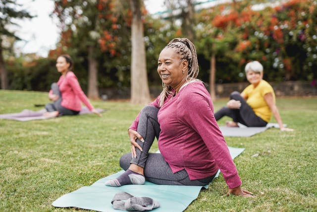 <p>Three middle-aged women do yoga together in a park</p>