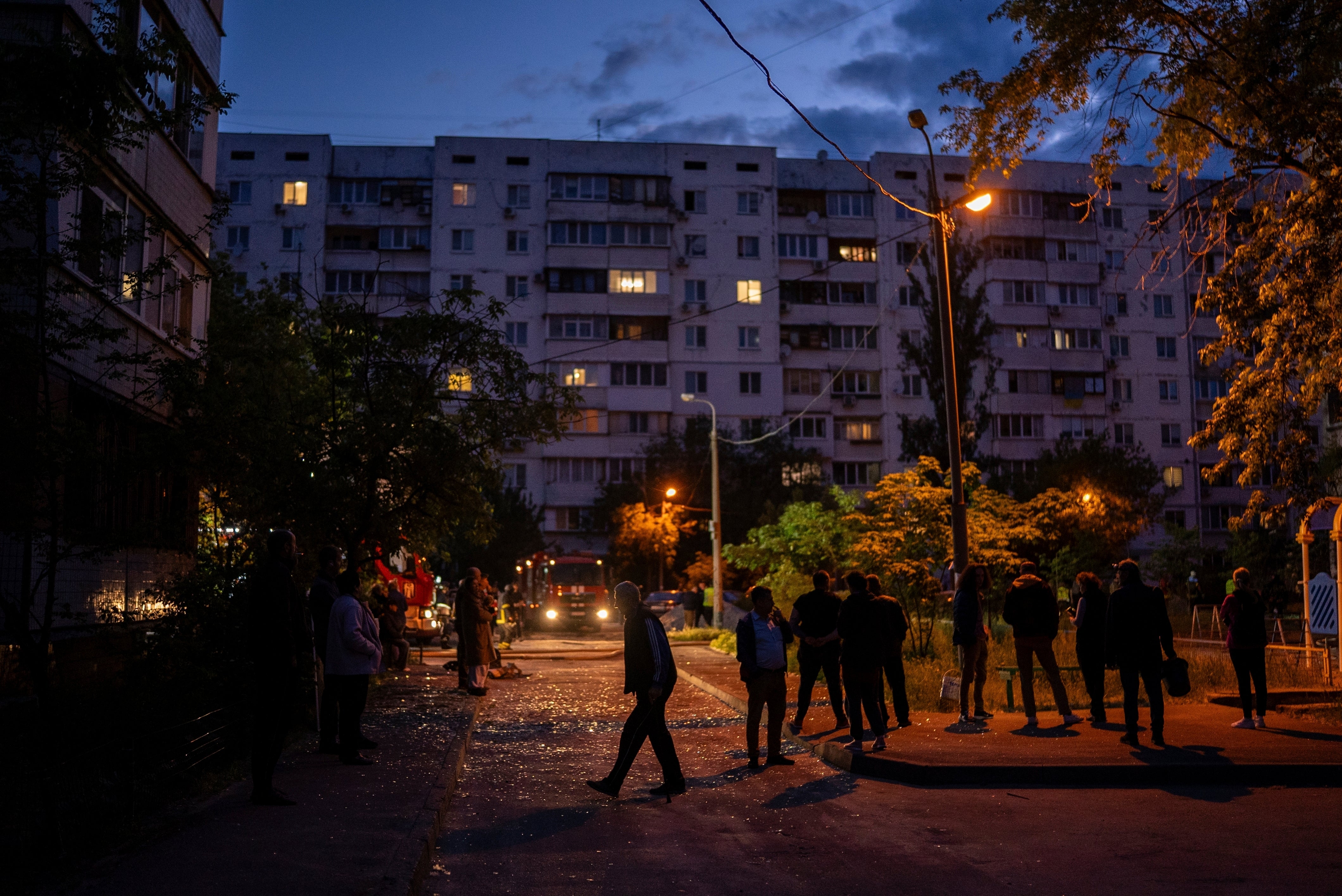 Local residents walk on a street with pieces of broken glass at the site of a residential building that was damaged after a Russian attack in Kyiv
