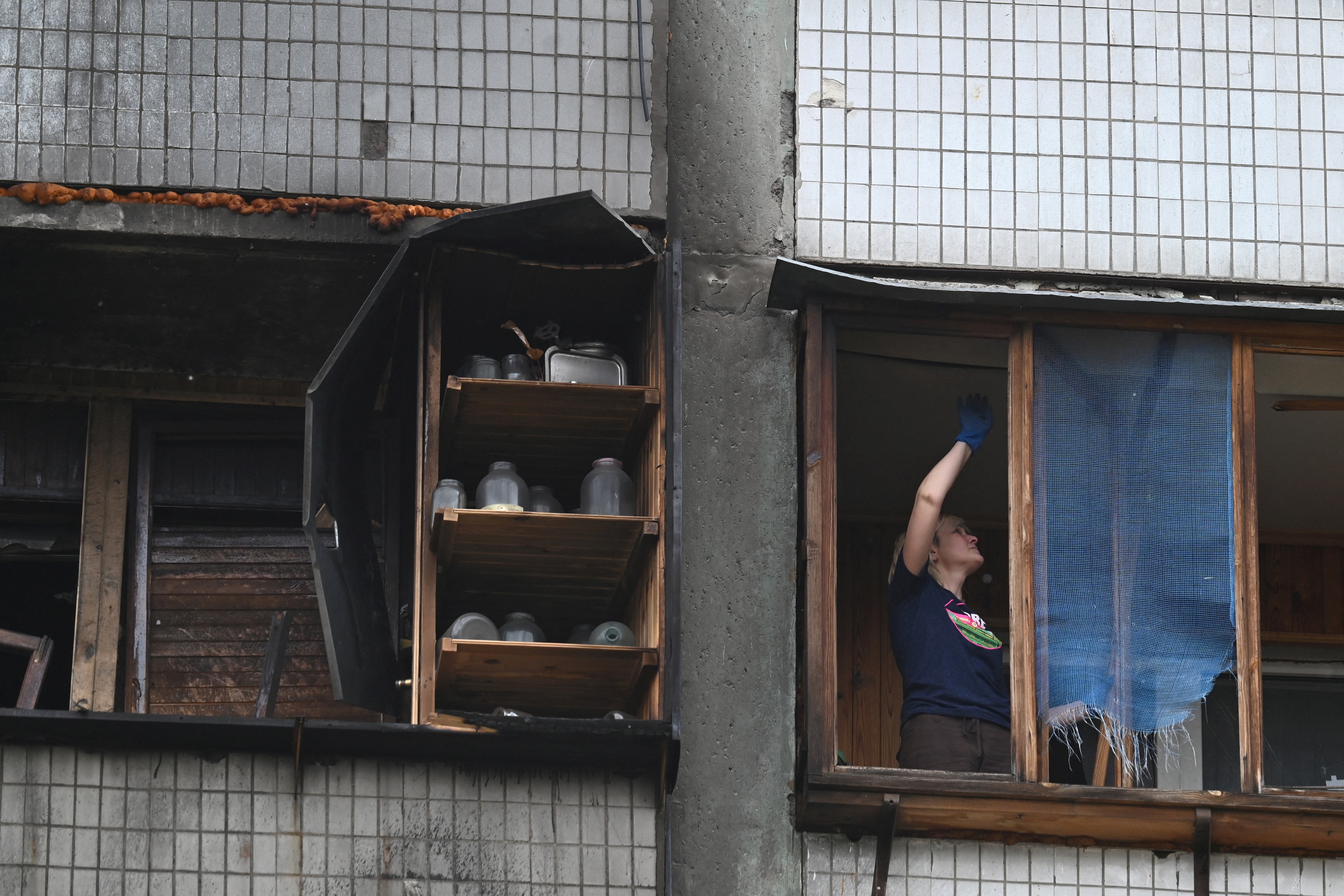 A local resident of a multistory residential building clears debris from her flat damaged following a Russian drone strike on Kyiv