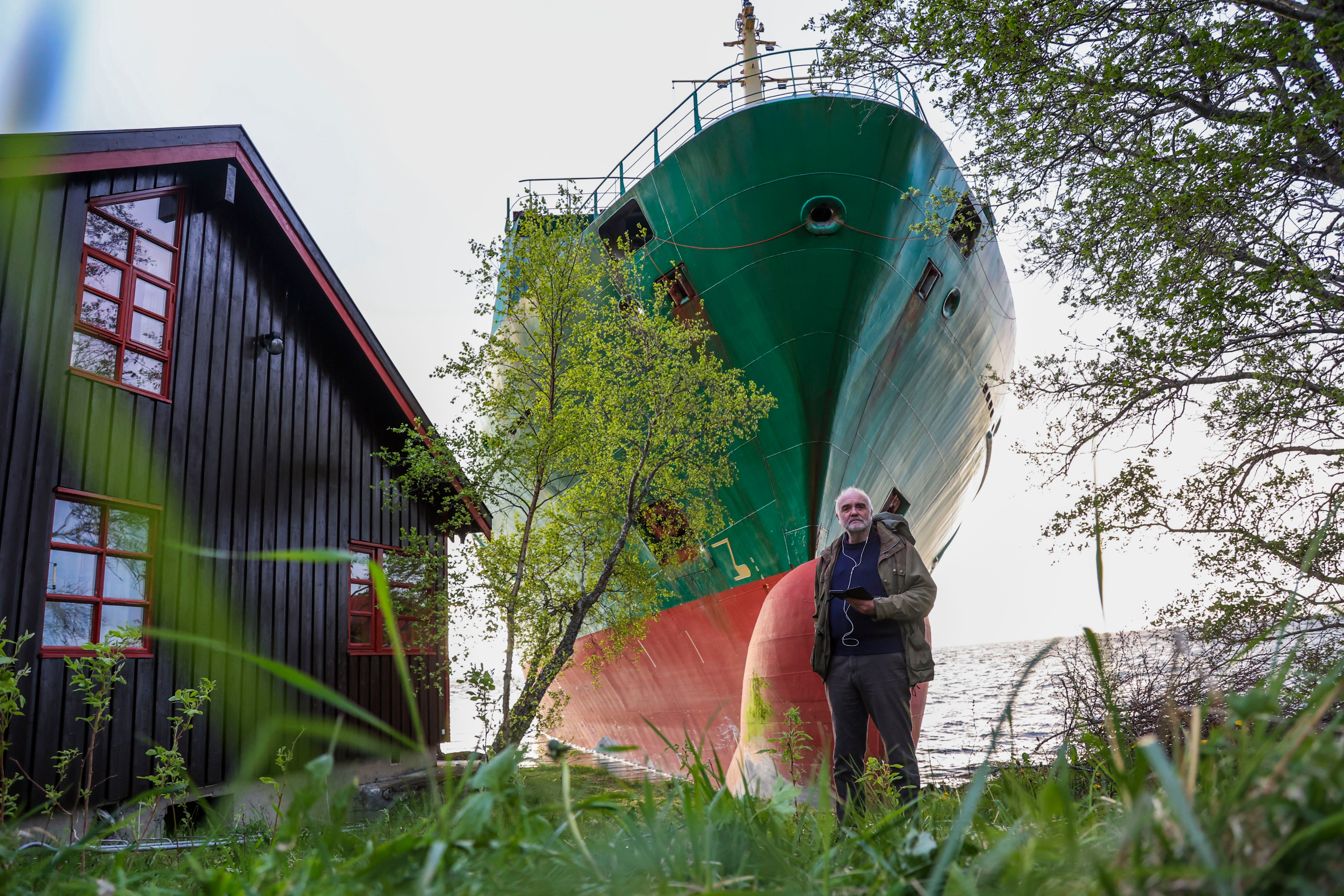 Johan Helberg stands next to his house, with the container ship NCL Salten in the background, after the 135-meter-long ship ran aground in the Trondheimsfjord, outside Byneset, in Trondheim, Norway, Thursday May 22, 2025. (Jan Langhaug/NTB Scanpix via AP)