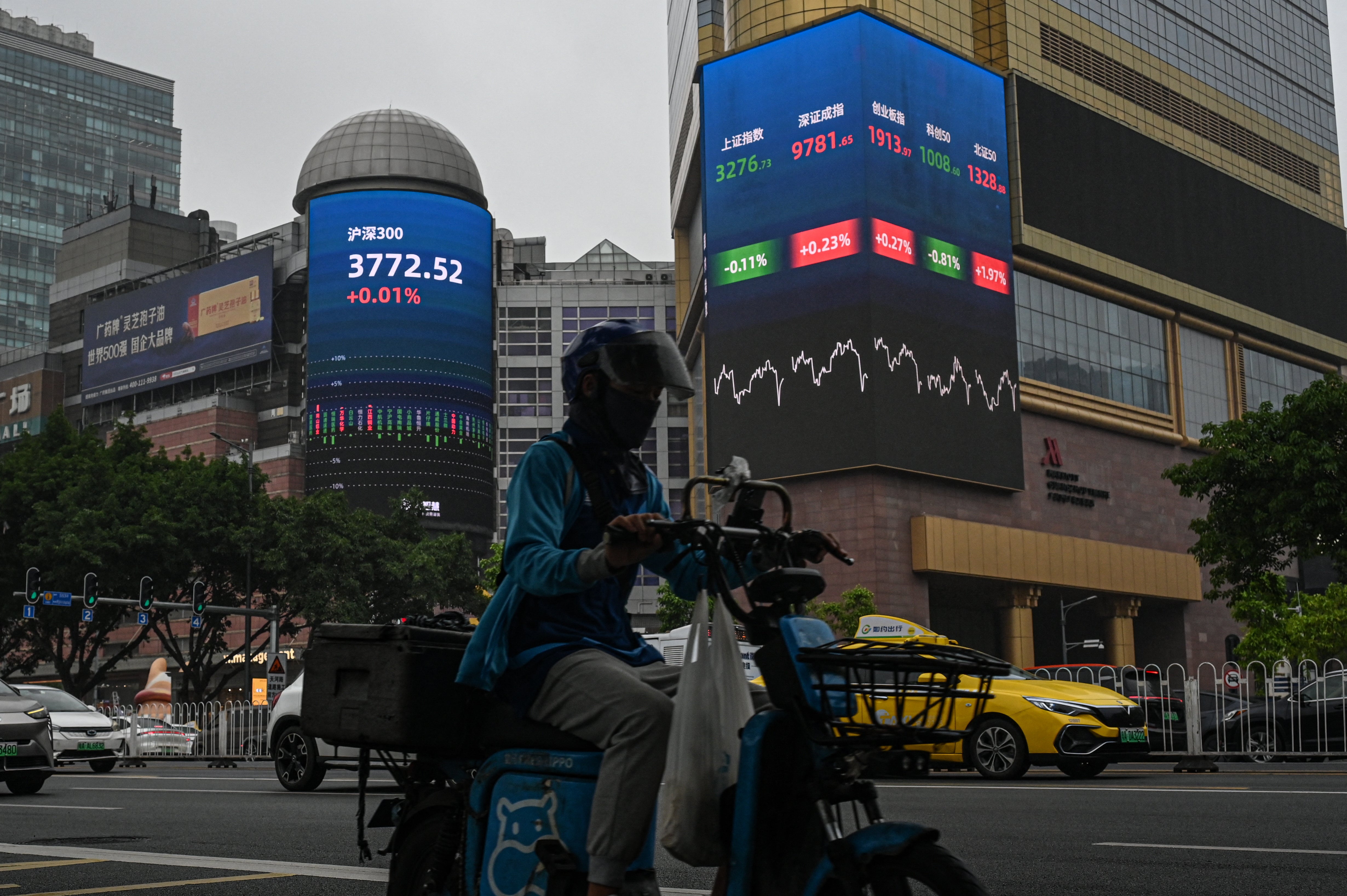 A delivery driver rides past screens showing stock market figures outside a shopping mall in Guangzhou in southern China