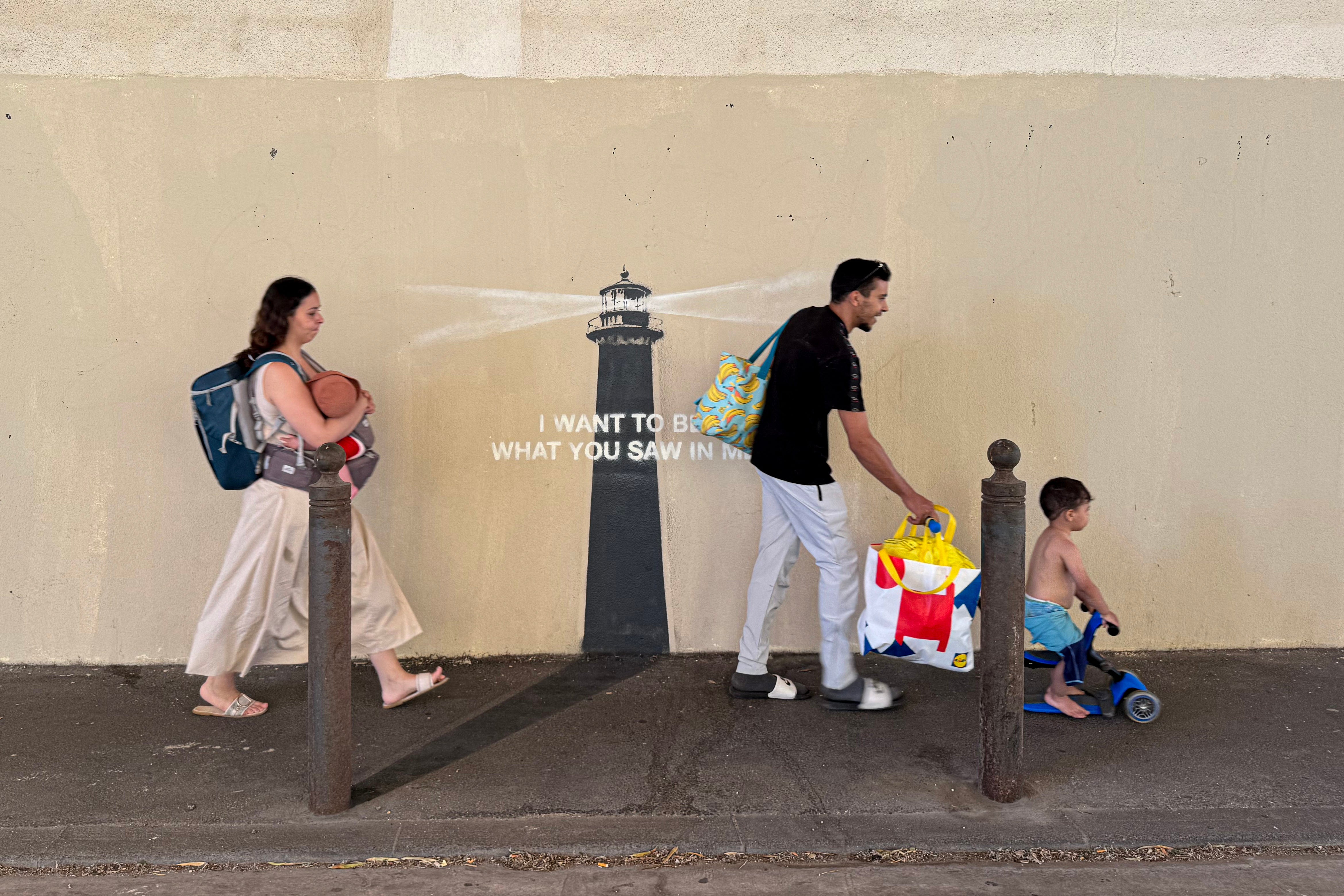 Pedestrians walk past a newly released artwork by street artist Banksy on the facade of a building in Marseille