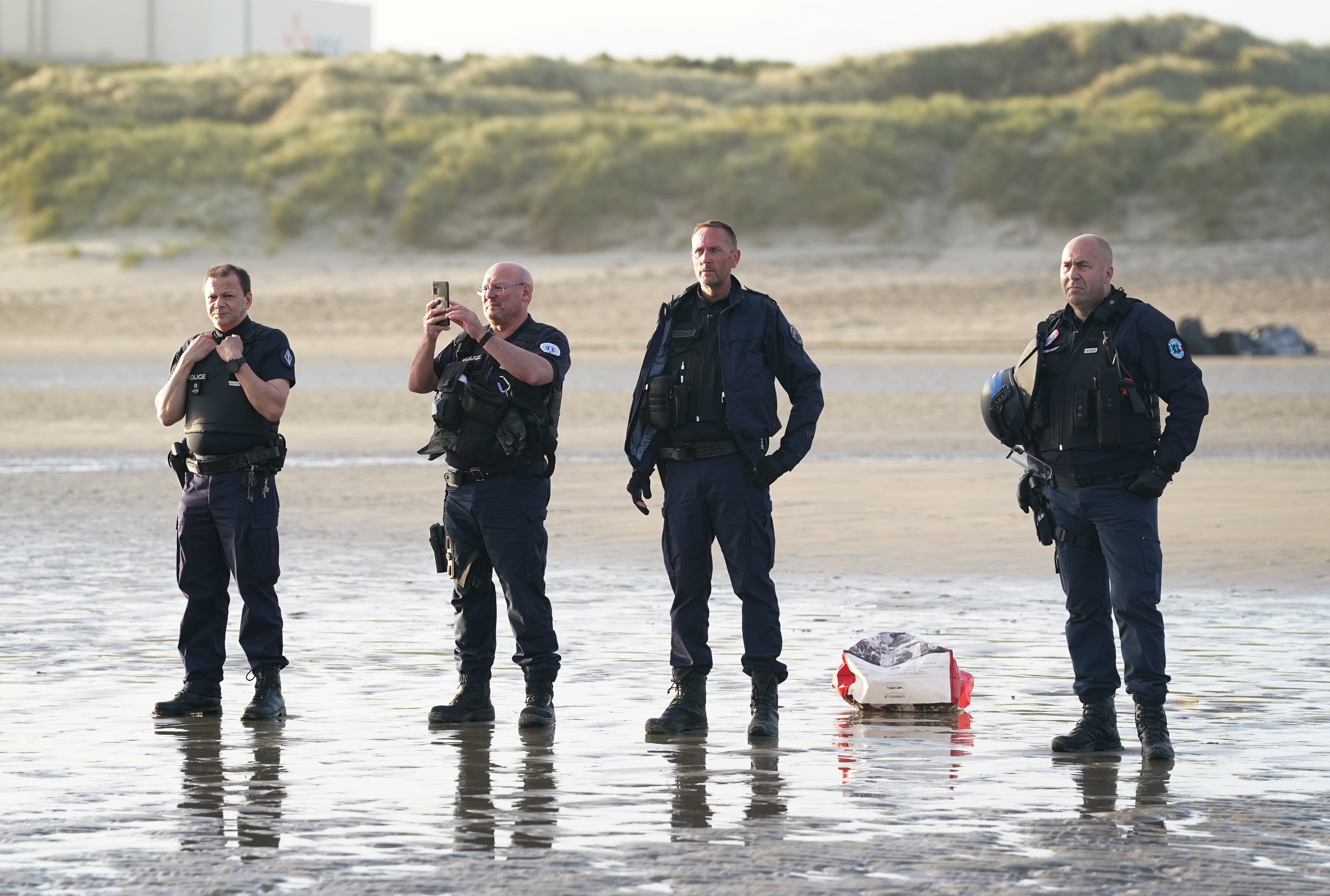 French police officers watch a group of people thought to be migrants board a small boat leaving the beach at Gravelines, France (Gareth Fuller/PA)