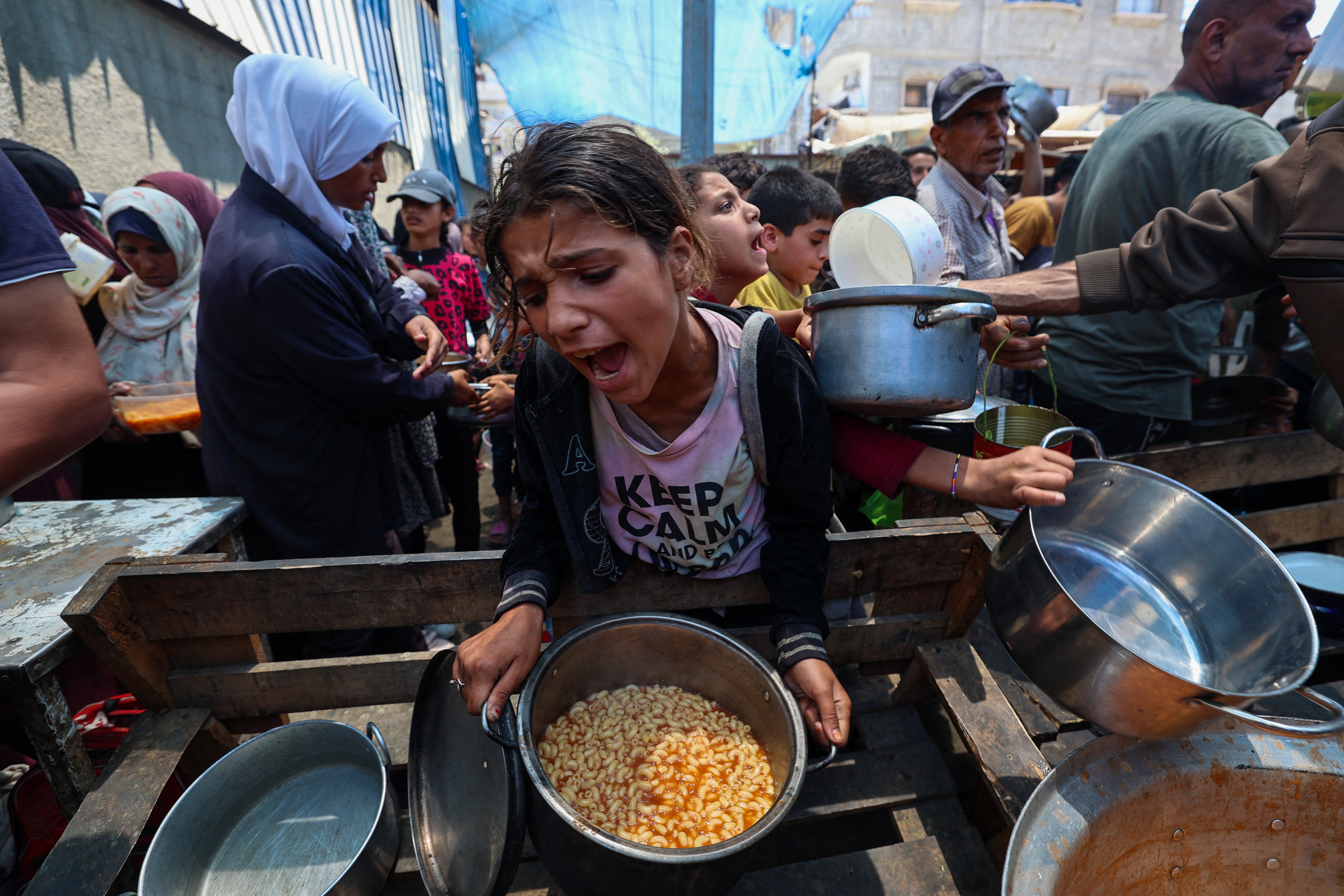 <p>A girl reacts after receiving a cooked meal as others wait at a distribution point in Nuseirat, central Gaza Strip</p>