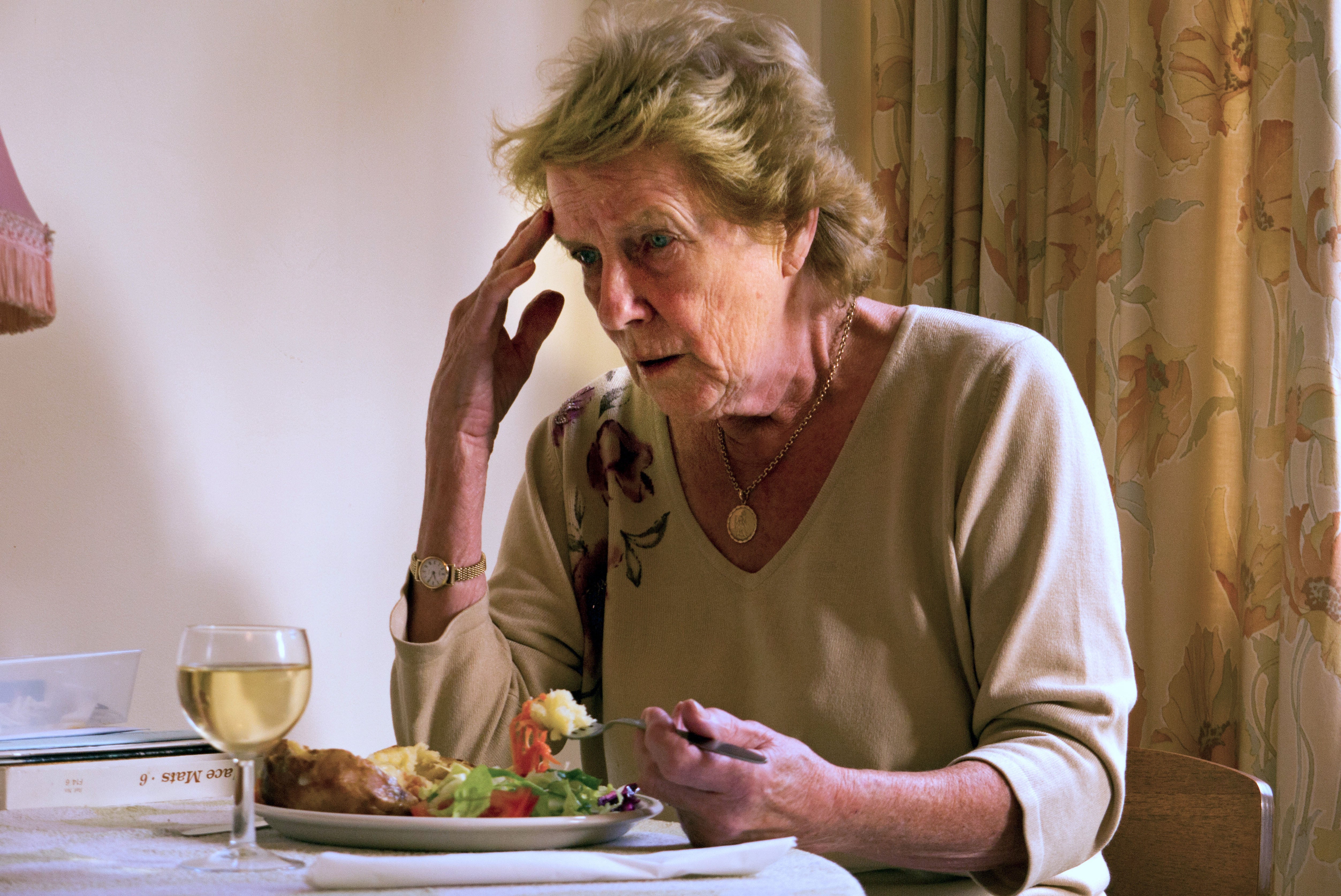 <p>An elderly woman with Alzheimer's Disease sitting in her home eating a meal looking confused and worried</p>