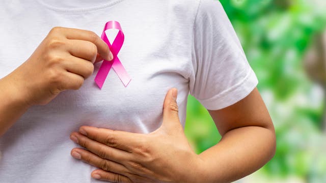 <p>Woman putting pink ribbon up to her breast to represent breast cancer</p>